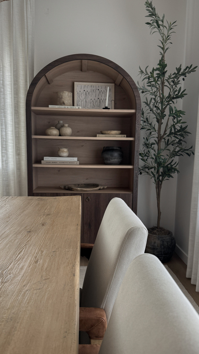 An organic modern dining room moment featuring a dark arched cabinet, warm wood tones, and a faux olive tree for height and contrast. The open shelves are styled with neutral ceramics, vintage-inspired books, and hand-thrown pottery pieces—creating a curated, layered look with Amazon finds that feel custom. Soft, upholstered dining chairs and tonal textures tie it all together in a calm, neutral palette.

Amazon home decor · organic modern dining room · arched cabinet styling · earthy ceramics · faux olive tree · neutral dining chairs · cozy minimalist decor · Amazon shelf styling · warm neutral interiors · organic textures and tones 

 

#LTKHome