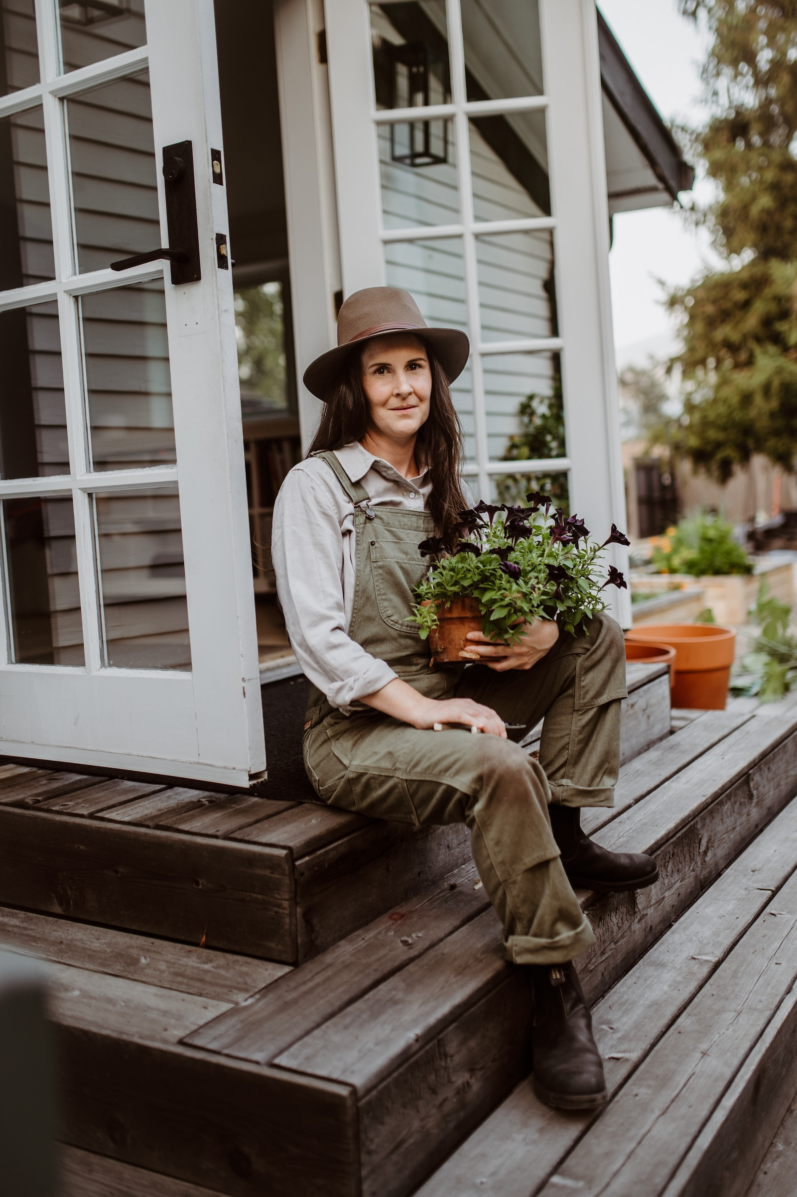 A quiet moment on the deck, giving these petunias a little TLC 🌿🍃 Cozy layers and green overalls are my fall gardening uniform—perfect for a day spent nurturing potted plants before winter. Sometimes, the best therapy is a pair of pruning shears and a well-loved deck. #PlantCare #HomeForTheHarvest #GardenStyle #LTKGarden #Gardening #Plants  

 #LTKHome