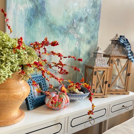 Decorate a white 3 drawer console table with fall accents. Featuring dried hydrangeas, orange bittersweet, blue and white Chinoiserie bowl, natural finish lanterns, decoupage pumpkins with orange Chinoiserie paper napkins.

#LTKSeasonal #LTKhome