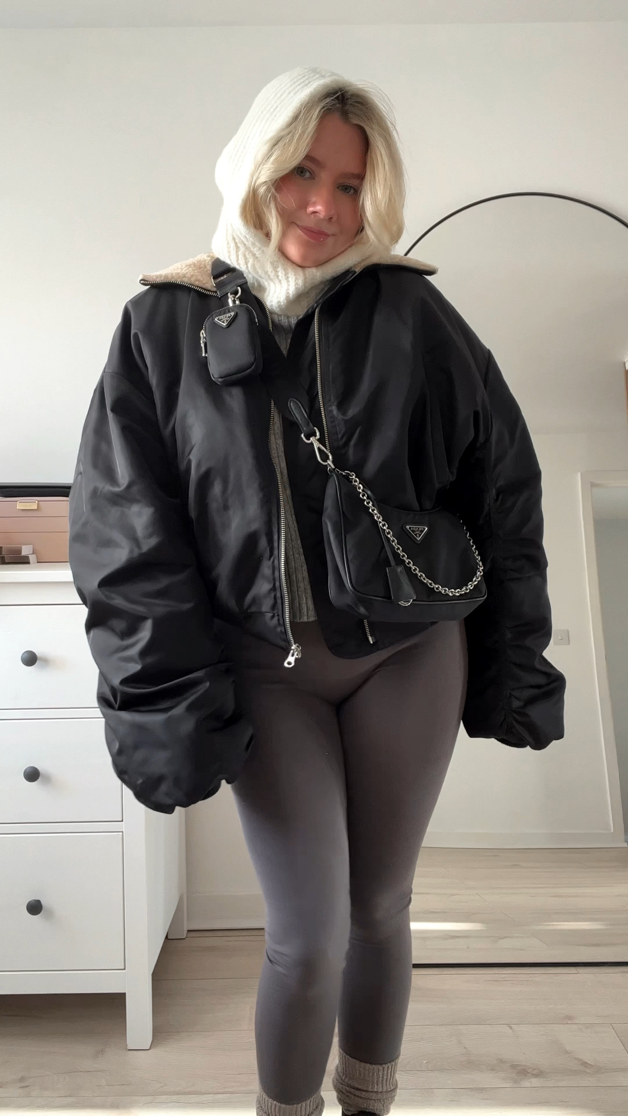 a cosy layered look featuring grey seamless fleece lined leggings, black chelsea chunky ankle boots, a white ribbed t-shirt, a grey ribbed high neck boxy sweater, black bomber jacket with borg collar, cream knit balaclava, black cross body prada bag and square sunglasses 

#LTKstyletip #LTKSeasonal #LTKeurope