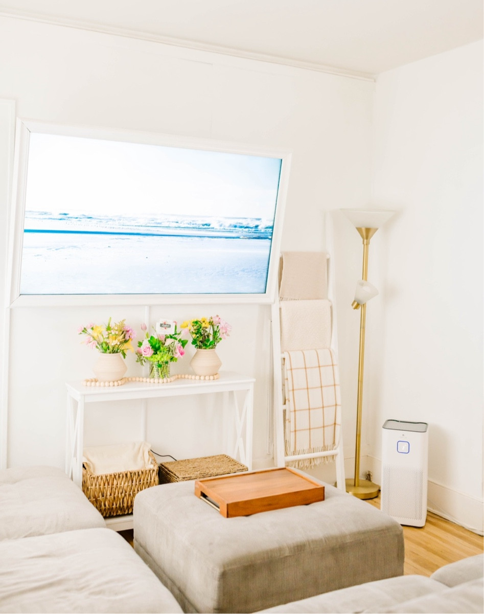 Warm and minimal living room with neutral colors gray couch, beach scene on TV white ladder with cozy, blankets, white entryway table under the TV, air purifier, lighting, clean

#LTKhome #LTKFind #LTKunder100