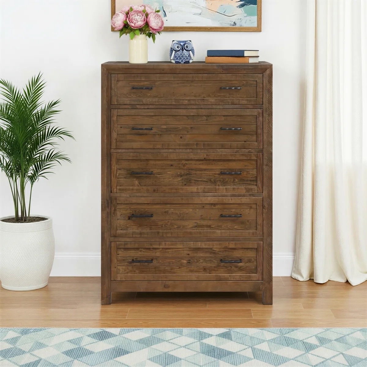 This solid wood 5-drawer dresser from Wayfair has that warm, collected look that makes a bedroom feel instantly more grounded. The rich brown wood grain, wide drawer fronts, dark metal pulls, and dovetail joinery give it a really substantial feel without looking too heavy. I like it styled with the potted palm, pink flowers, stacked books, abstract wall art, soft curtains, and blue geometric rug. It’s currently marked 32% off at Wayfair