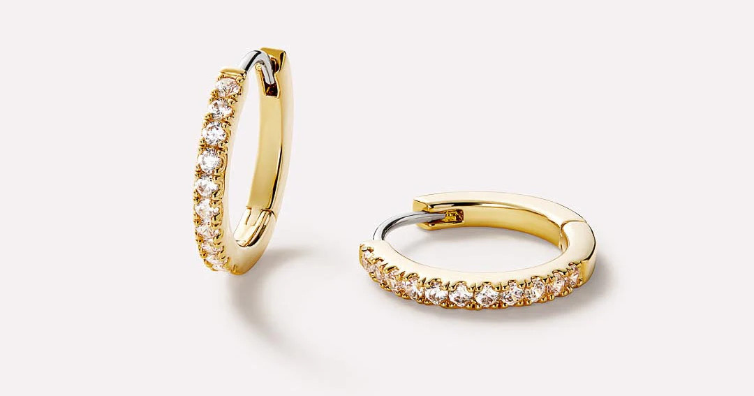 Made with tarnish-proof 14k gold plating and a stunning row of gems, these gold huggie hoops fit ... | Ana Luisa