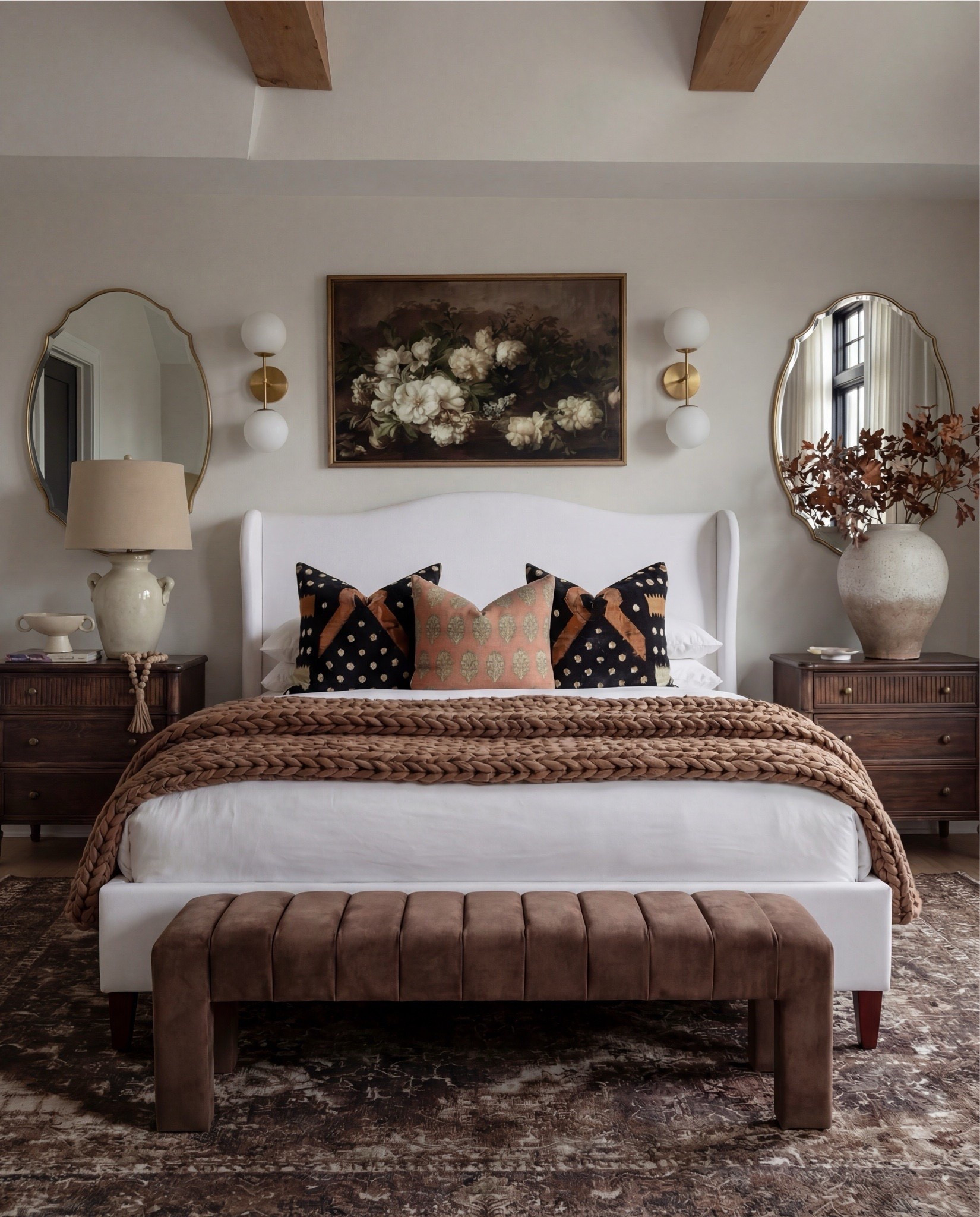 This bedroom feels warm, layered, and quietly refined. The soft upholstered bed keeps the space light and serene, while rich wood tones, earthy textiles, and vintage-inspired accents add depth and contrast. Sculptural lighting, warm brass details, and cozy textures create a balance between elegance and comfort — a space that feels elevated yet deeply livable.

The styling leans into warm neutrals and organic materials — chunky knits, aged woods, soft linen layers, and curated decorative moments that give the room a collected, timeless atmosphere.

Shop the Look:
• White upholstered wingback bed frame
• White cotton duvet cover + pillow shams
• Textured throw pillows (rust + black patterned)
• Chunky knit throw blanket (warm brown)
• Vintage-style brown area rug
• Dark wood nightstands with brass knobs
• Ceramic table lamp (neutral glaze)
• Brass globe wall sconces
• Framed floral artwork (muted tones)
• Arched brass wall mirrors
• Upholstered bench at foot of bed (camel brown)
• Cream accent chair with wood arms
• Black fluted dresser with brass pulls
• Round black fluted end table 
•Fecor books 
• Large ceramic floor vase (earthy clay tone)
• Decorative wood bead garland
• Sheer white curtain panels
•Round decor bowl tray 
•Wood jewellery box 
•Terracotta bowl 
@Wayfair 

#LTKSaleAlert #LTKHome
