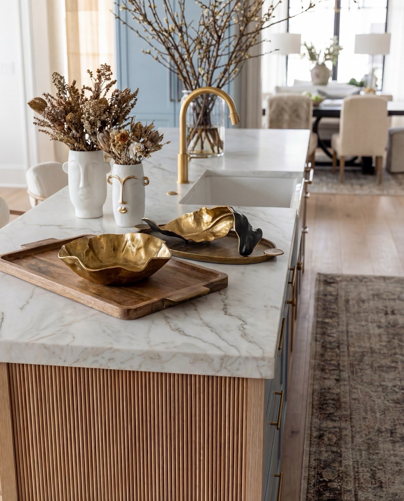 Shop the Look:
• Soft blue shaker-style kitchen cabinets
• White marble countertops & backsplash (warm veining)
• Slatted wood kitchen island paneling (light oak)
• White globe pendant lights (brass stem)
• Brass kitchen faucet + brass cabinet hardware
• Boucle counter stools with light wood frame
• Black gas range
• Vintage-style runner rugs (neutral taupe + faded pattern)
• Sculptural gold decorative bowls
• Wooden serving tray (warm walnut tone)
• White sculptural ceramic vases with dried florals
• Glass vase with branch arrangement

#LTKSpringSale #LTKHome #LTKSaleAlert