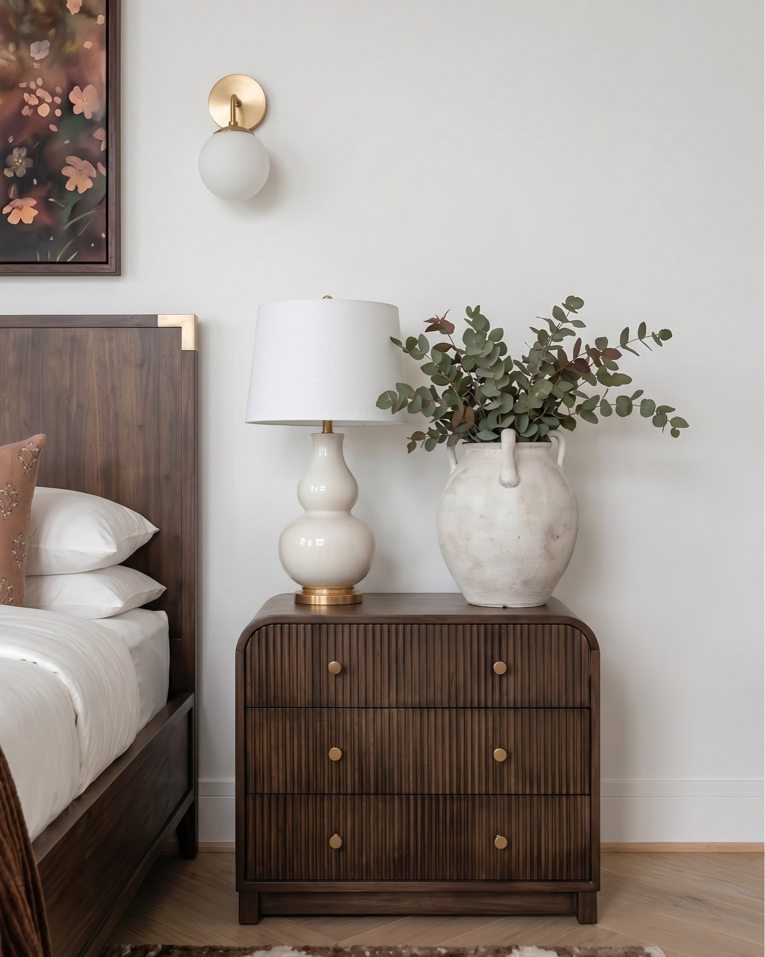 Warm modern bedroom design featuring a rich wood bed frame with brass accents, styled with crisp white bedding, textured neutral throw blanket, and terracotta accent pillows for a cozy, elevated look. A plush upholstered bench adds softness at the foot of the bed, layered over a geometric brown and cream area rug.
Matching wood nightstands with fluted detailing are styled with ceramic table lamps, decorative vases, and stacked books for a balanced, designer feel. Above the bed, a statement abstract art piece ties together warm earthy tones, complemented by modern brass wall sconces.
The space continues with a coordinating fluted wood dresser styled with neutral ceramic decor, a framed botanical print, a glass hurricane candle holder, and a decorative tray with small accessories. A cozy accent chair with soft upholstery and wood frame pairs perfectly with a matching round side table, topped with a candle for a warm, inviting touch.
 modern bedroom furniture, warm neutral bedroom decor, wood bed frame, upholstered bench, fluted dresser, designer nightstand styling, ceramic table lamps, abstract wall art, brass wall sconces, cozy accent chair, neutral home decor, earthy tone bedroom, luxury bedroom styling, high-end furniture look for less, transitional modern decor.

#LTKsale #LTKhome