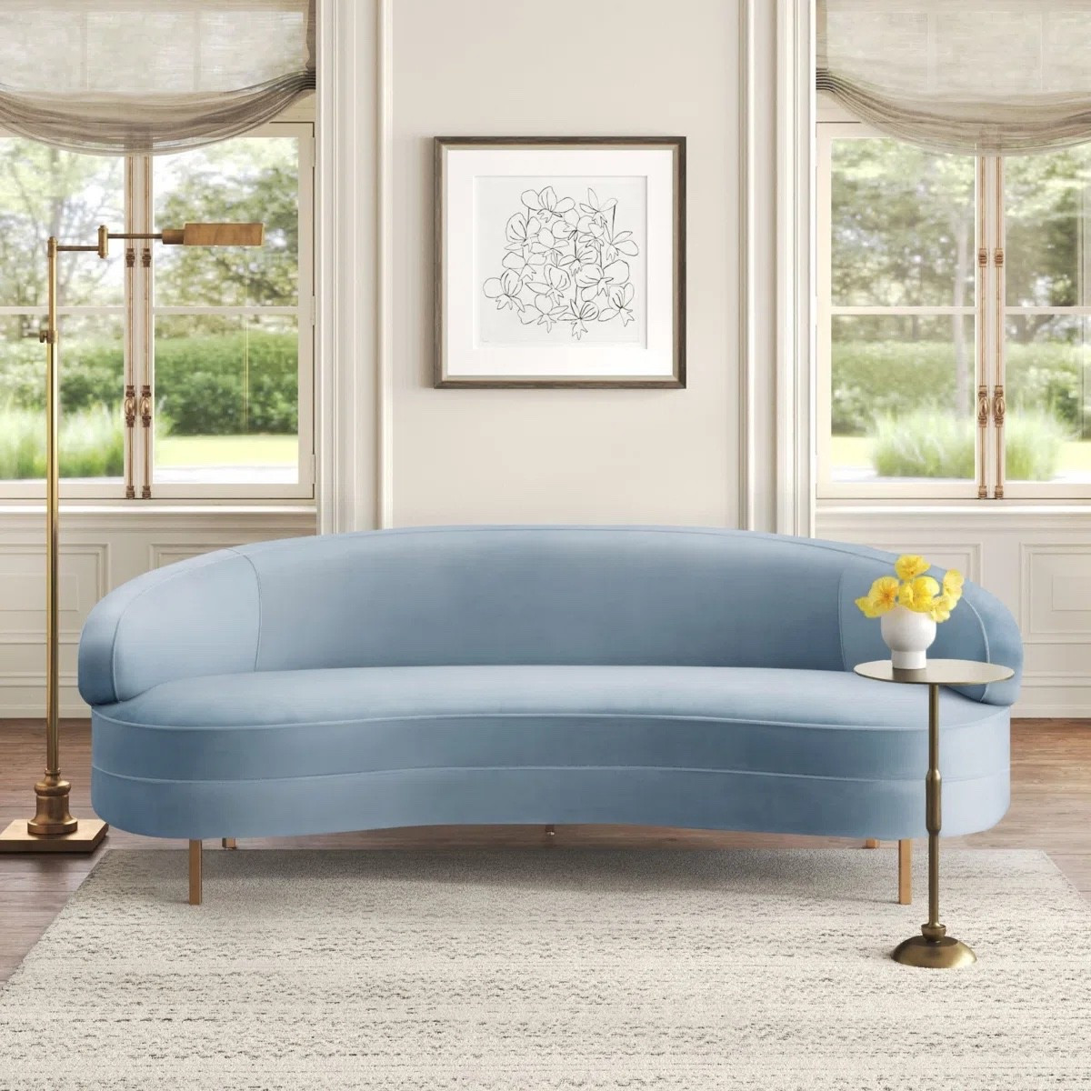 This curved upholstered sofa from Wayfair is the perfect statement piece for a modern living room. With its soft blue fabric and elegant silhouette, it adds both comfort and style. Paired with a textured area rug, gold floor lamp, side table, and minimal wall art, it creates a bright and sophisticated space. 
