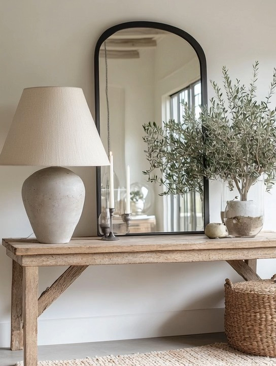 Create a simple yet elevated console table moment that instantly brings calm, balance, and quiet luxury into your home. This timeless look is built around an oversized table lamp—a major design trend right now—paired with a black-framed mirror to add depth, contrast, and architectural interest. A mini olive tree introduces organic texture and softness, grounding the space and making it feel lived-in yet refined. The beauty of this console setup is its flexibility: mix and match lamp shapes, swap mirror frames, or layer in different natural elements to recreate the same elegant effect in an entryway, hallway, living room, or bedroom. Clean lines, natural materials, and thoughtful styling turn this console table into a modern statement that feels both curated and effortless.
#consoletable #modernhome #quietluxury 

 #LTKHome
