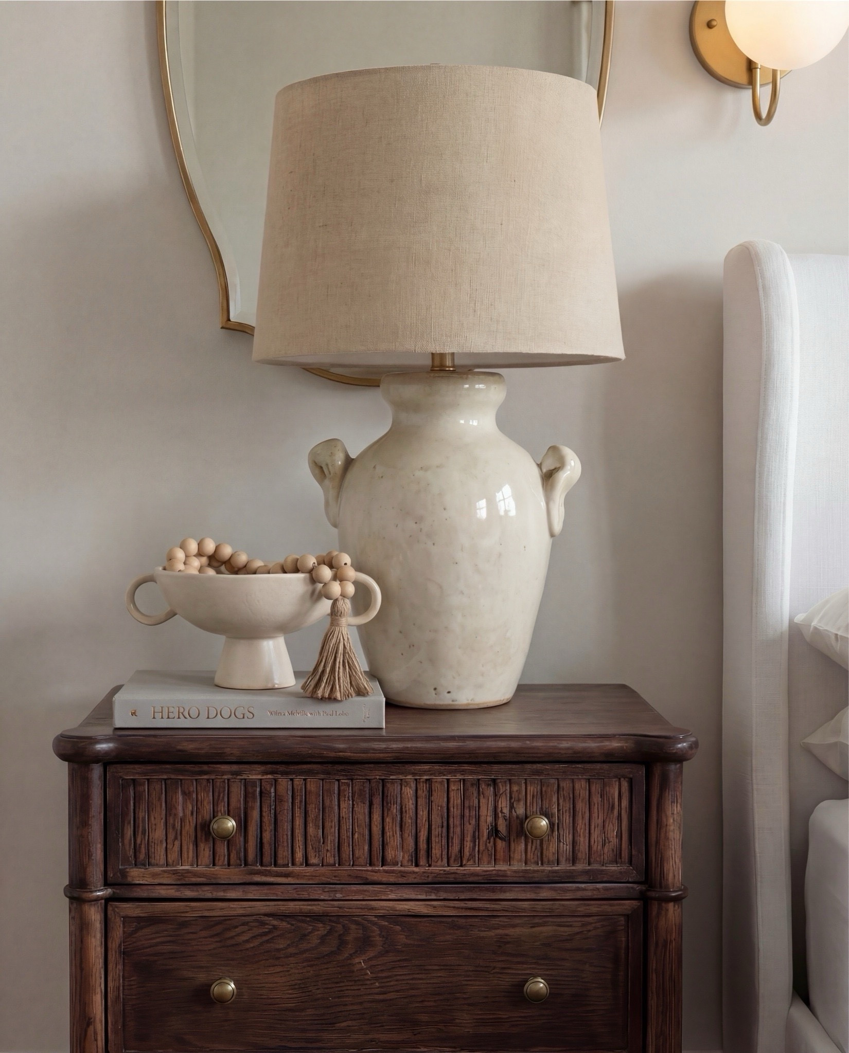 Shop the Look:
• White upholstered wingback bed frame
• White cotton duvet cover + pillow shams
• Textured throw pillows (rust + black patterned)
• Chunky knit throw blanket (warm brown)
• Vintage-style brown area rug
• Dark wood nightstands with brass knobs
• Ceramic table lamp (neutral glaze)
• Brass globe wall sconces
• Framed floral artwork (muted tones)
• Arched brass wall mirrors
• Upholstered bench at foot of bed (camel brown)
• Cream accent chair with wood arms
• Black fluted dresser with brass pulls
•Ceramic beige decor bowl
•Decor wood beads 
•Decor book
• Large ceramic floor table vase (earthy clay tone)
• Decorative wood bead garland
• Sheer white curtain panels
•Decor tray
•Hurricane candle holder
Wood Jewelery box 


#LTKSaleAlert #LTKHome