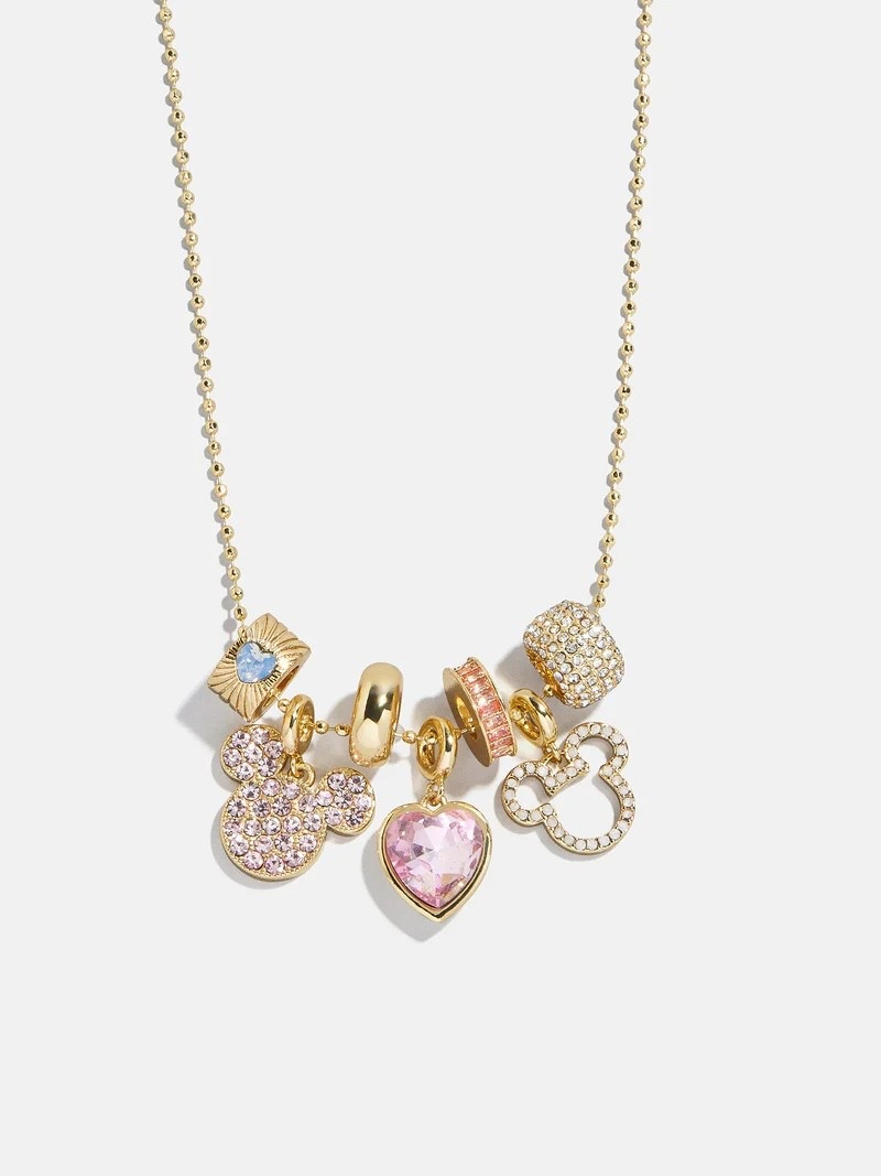 This brand NEW Valentine’s gold-tone charm necklace has a soft, romantic Disney vibe!
It features a delicate beaded gold chain adorned with a curated mix of charms, including:
    •    A pink crystal heart pendant as the centerpiece
    •    A pavé Minnie head charm with blush-toned crystals
    •    A gold outline Minnie charm for a subtle Disney touch
    •    Sparkling crystal-encrusted barrel and spacer charms
    •    Soft pastel accents that give it an elegant, feminine finish
Overall, it feels sweet, polished, and collectible — perfect for Disney fans who love subtle sparkle and charm-style jewelry that layers beautifully with other necklaces.
