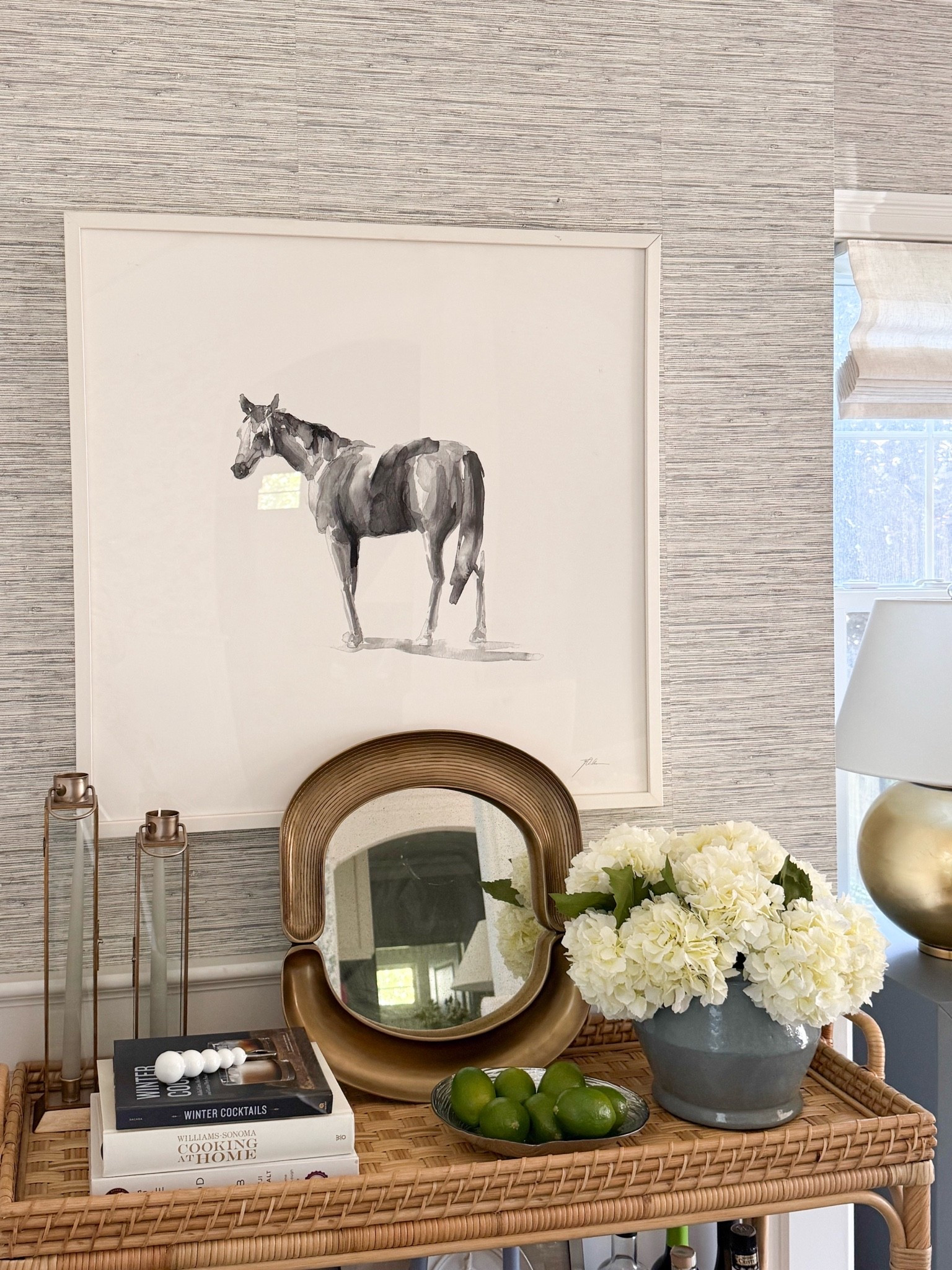 One of my favorite styled corners in the house! The horse artwork, sculptural brass mirror, white hydrangeas, and woven console bring together so many of the details I love. A beautiful mix of classic pieces and natural textures that feels collected and timeless.

horse wall art, woven console table, rattan furniture, brass mirror, faux white hydrangeas, console table styling, dining room decor, grasscloth wallpaper, classic home decor, coffee table books, modern coastal interiors, girlonthehudson