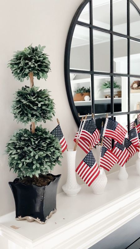 Simple patriotic fireplace mantle. Milk glass bud vases. Faux boxwood topiaries. Mini American flags. Large round mirror.

#LTKstyletip #LTKSeasonal #LTKhome