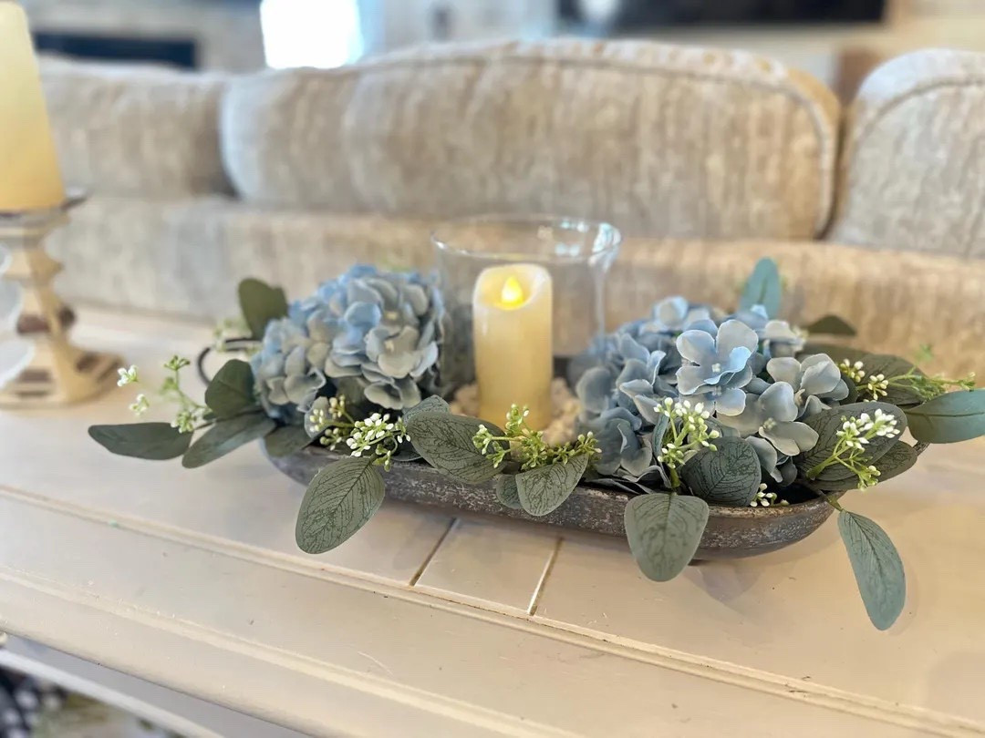 Create a warm and inviting focal point with this handcrafted rustic floral centerpiece by CountryHomeandHeart. Featuring lush greenery, soft blue hydrangeas, and a glowing LED candle nestled in a glass holder, all set within a beautifully distressed metal tray, this piece brings effortless elegance to any space. Perfect for coffee tables, dining rooms, or entryways, it adds a cozy farmhouse feel while remaining timeless and versatile for any season. #LTKHome #FarmhouseDecor #TableCenterpiece #HydrangeaLove #CozyHome #RusticStyle #HomeStyling #NeutralDecor

#LTKSeasonal #LTKHome #LTKWedding