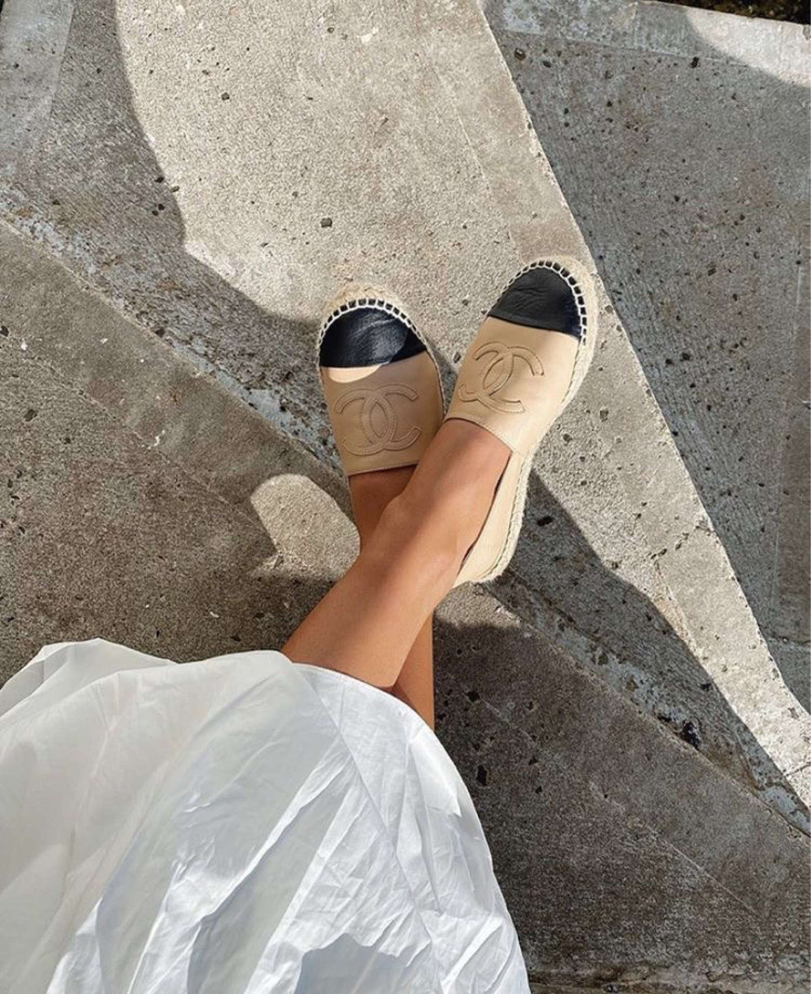Beige and black Chanel espadrilles worn on sunlit stone steps.