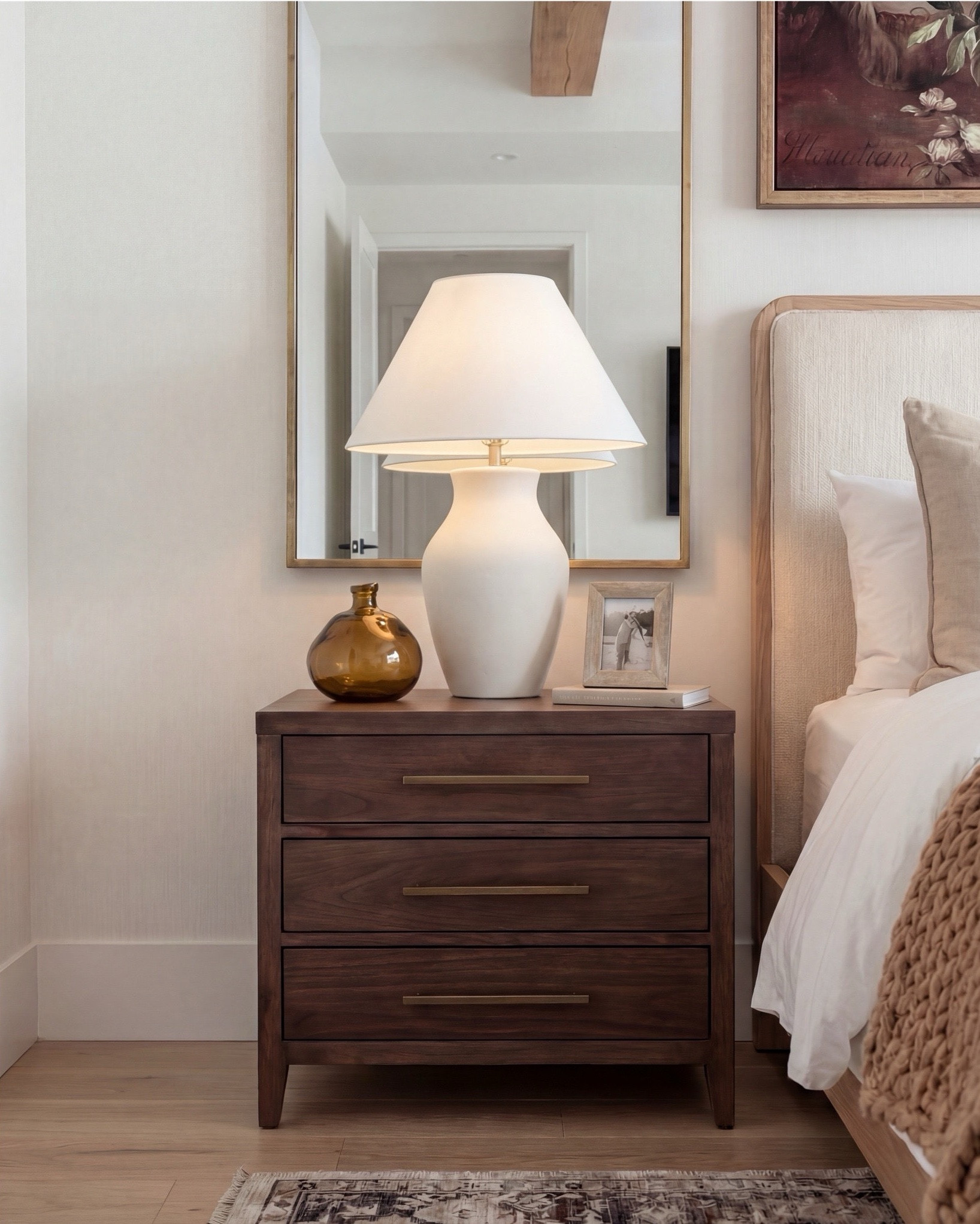 Shop the Look: Bedroom Refresh
• Upholstered bed frame (light neutral fabric)
• White cotton duvet cover + pillow shams
• Neutral patterned area rug
• Chunky knit throw blanket (warm beige)
• Woven knit poufs (foot-of-bed seating)
• Dark wood nightstands with brass pulls
• Sculptural white ceramic table lamps
• White tapered lamp shades
• Brass-framed rectangular mirrors
• Framed floral artwork (warm, moody tones)
• Neutral linen accent pillows
• Ceramic decorative bowl (white sculptural style)
• Small glass vase with white florals
• Dark wood dresser
• Wood upholstered accent chair 
• Brass tray
• Black leaf decor
• Brown wall art

#LTKhome #LTKsale #LTKstyletip