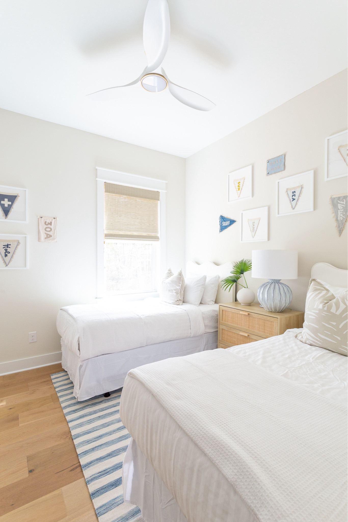 The bunk room bedroom at Hola Beaches Casita! Includes wavy upholstered headboards, blue striped rug, Florida and beach pennants in white gallery frames, a rattan nightstand, 
 a white and brass ceiling fan, and palm print pillows! Get more details and see the full tour here: https://lifeonvirginiastreet.com/hola-beaches-casita-30a-tour/.
.
#ltkhome #ltkseasonal #ltksaleslert #ltkfindsunder50 #ltkfindsunder100 #ltkstyletip #ltktravel 30A decor style

#LTKHome #LTKSaleAlert #LTKSeasonal