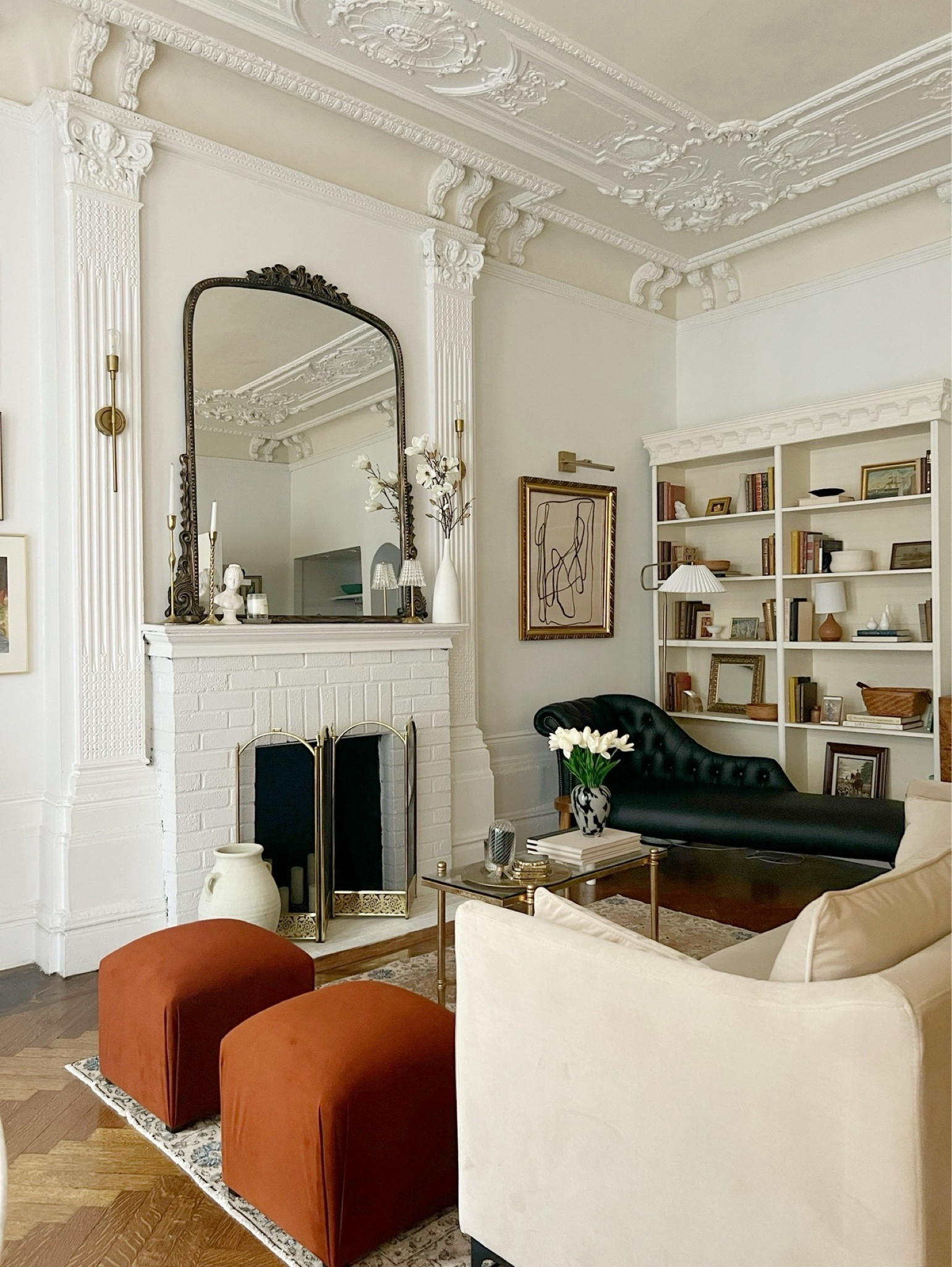 Studio/ living room links. Sand, velvet sofa, Ottomans, small, rectangular glass and gold, coffee table, black, leather shades, gold sconces, gold, picture, light, framed, abstract, art, floor lamp with pleaded lampshade.