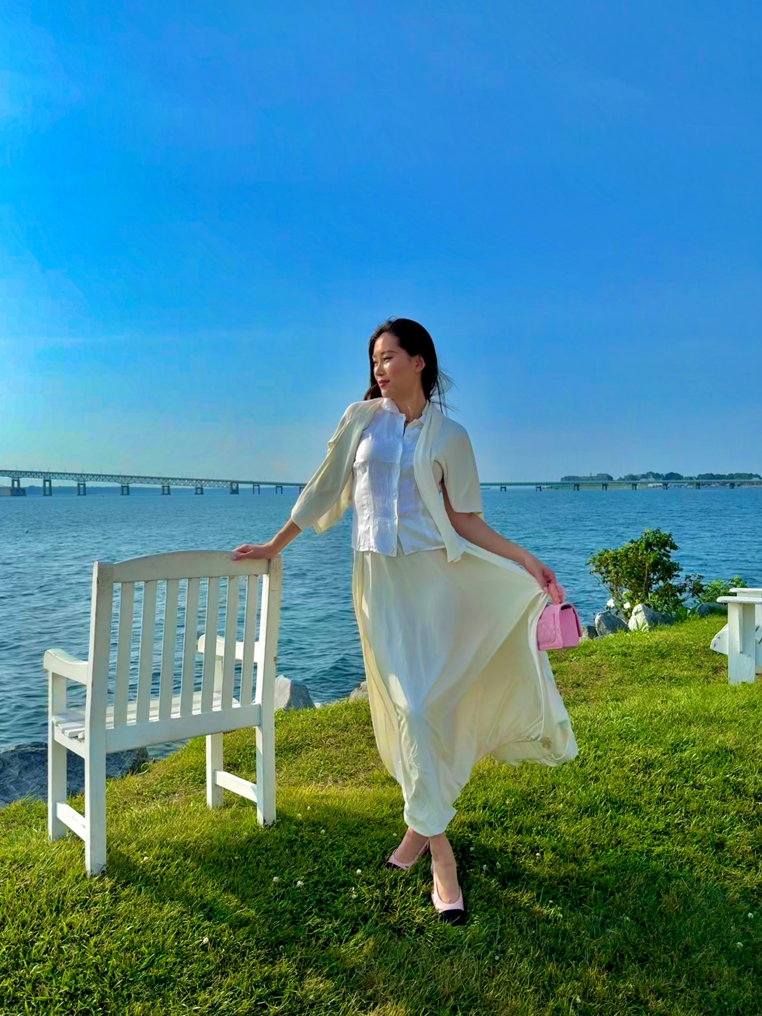 a white linen button-up paired with a cream silk maxi skirt and matching cardigan draped over the shoulders, styled with a pink chanel flap bag and pink-and-black chanel cap-toe ballet flats for a breezy waterfront afternoon in newport. the soft cream palette and heritage-coded chanel styling make this the perfect young old money summer outfit. perfect for newport getaways, coastal preppy afternoons, east coast summer trips, and quiet luxury vacation dressing. shop this look linked above.