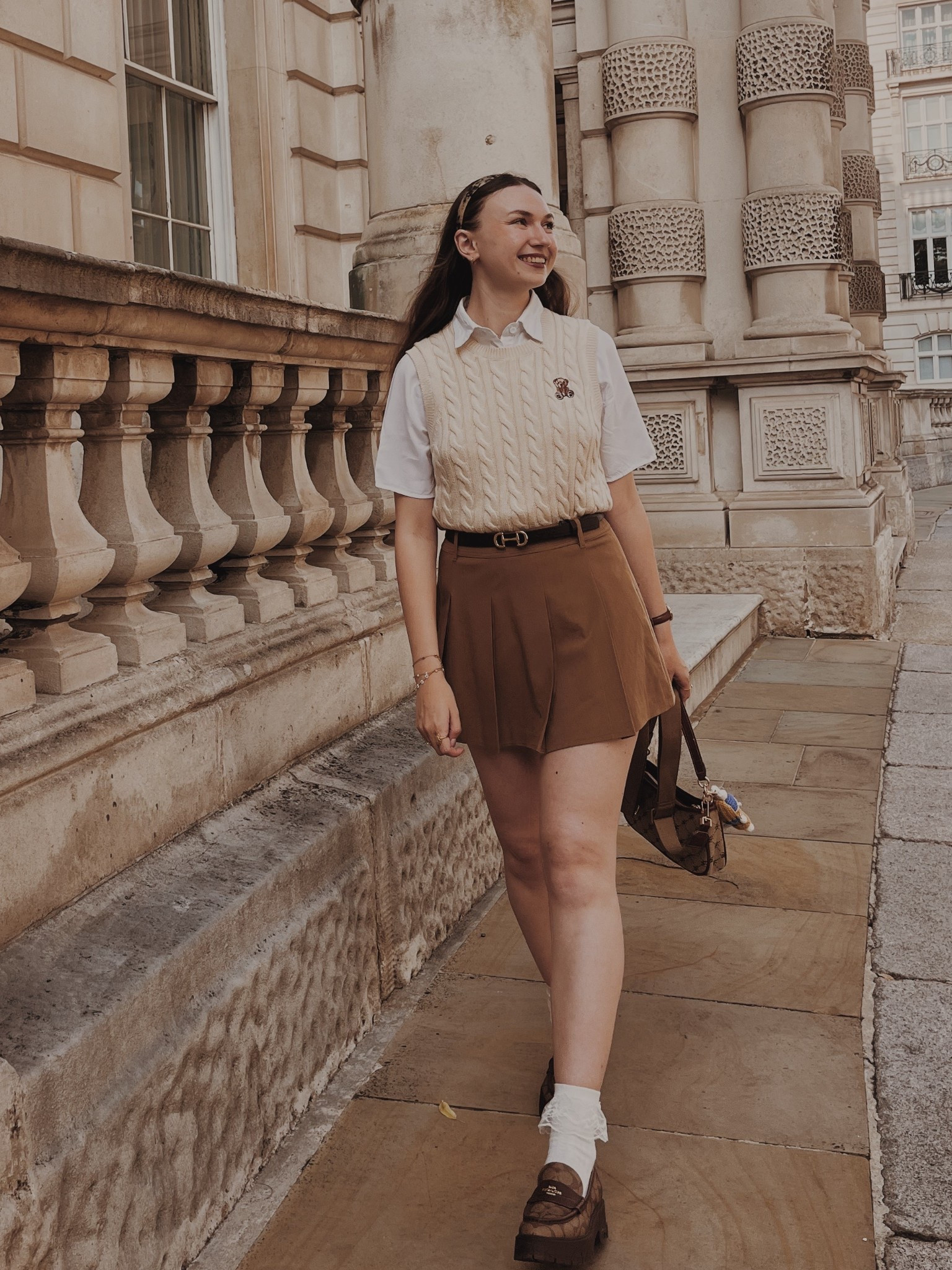 White short sleeved shirt
Beige cable knit sweater vest with bear detailing 
Camel skort 
Brown leather belt with horse bit buckle 
High heels loafers with pattern 
Tortoise headband

Light academia
Light academia outfit Light academia style Light academia aesthetic
Neutral outfit Autumn outfit
Autumn fashion
Autumn fashion inspo

#LTKSeasonal #LTKTravel #LTKShoeCrush