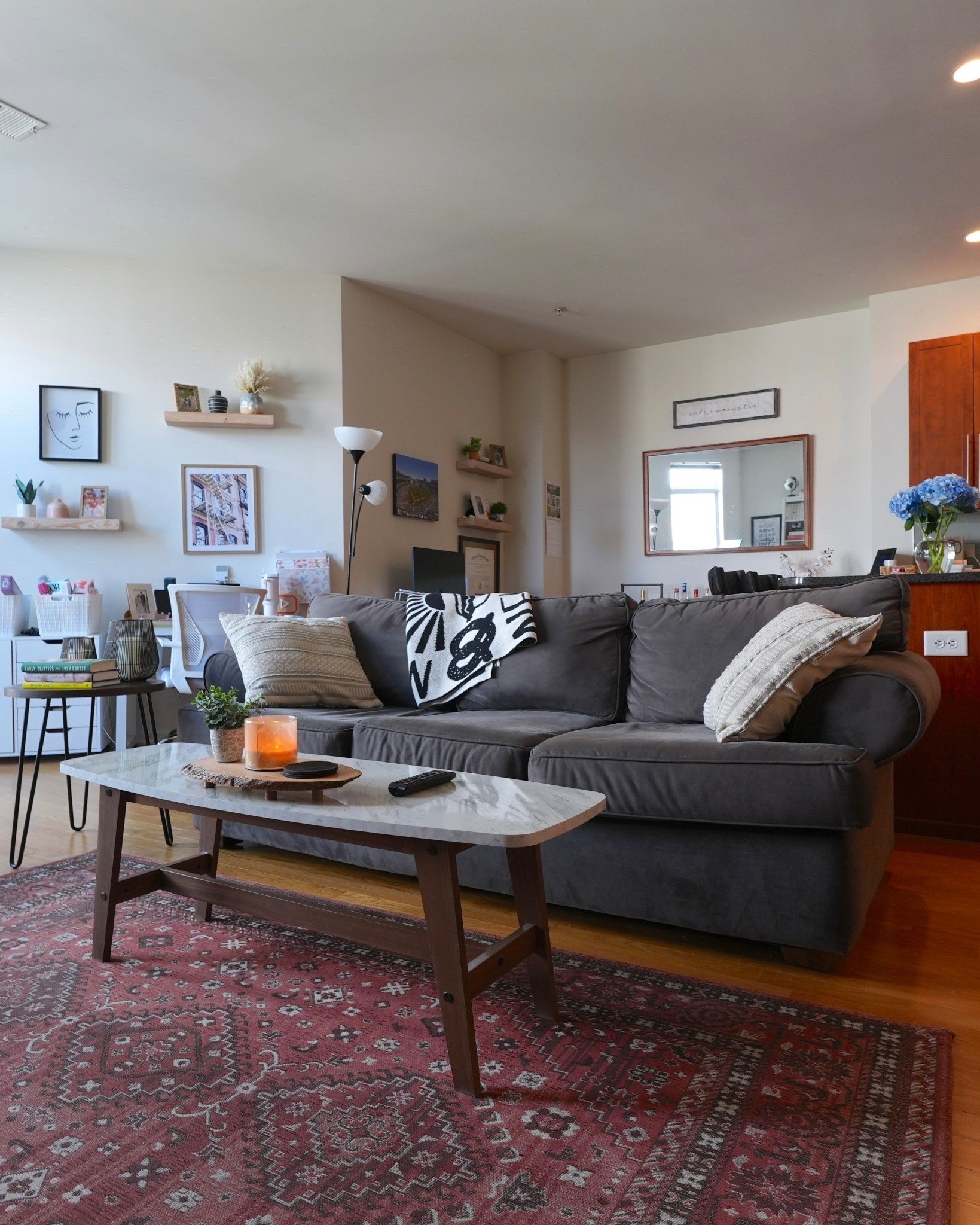 Here’s another angle of the living room! You can see how the gray sectional and coffee table anchor the space, while the red patterned rug adds color and warmth. I love having the TV mounted on the wall so the media console can hold baskets and decor instead of clutter. A floor lamp and side table make this the perfect cozy corner for reading or movie nights.

#LTKHome #LTKFindsUnder100