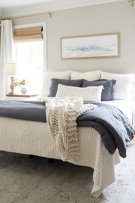 How to Make a Bed like in the magazines! Our bedroom is decorated for warmer months and includes a four poster bed with greige walls, farmhouse nightstand, blue linen duvet cover, ivory pickstitch quilt, vintage-style rug,  ivory linen curtains, bamboo shades, brass curtain rods and coastal art!

#LTKhome