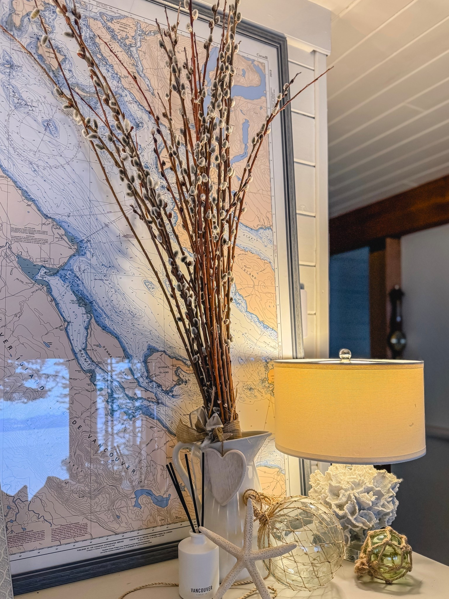 Simple late winter decor focused on white coastal accents. Pussy willows add a touch of spring. Love how the ocean view is reflected in the nautical chart’s glass  

#LTKwinter #LTKstyletip #LTKhome