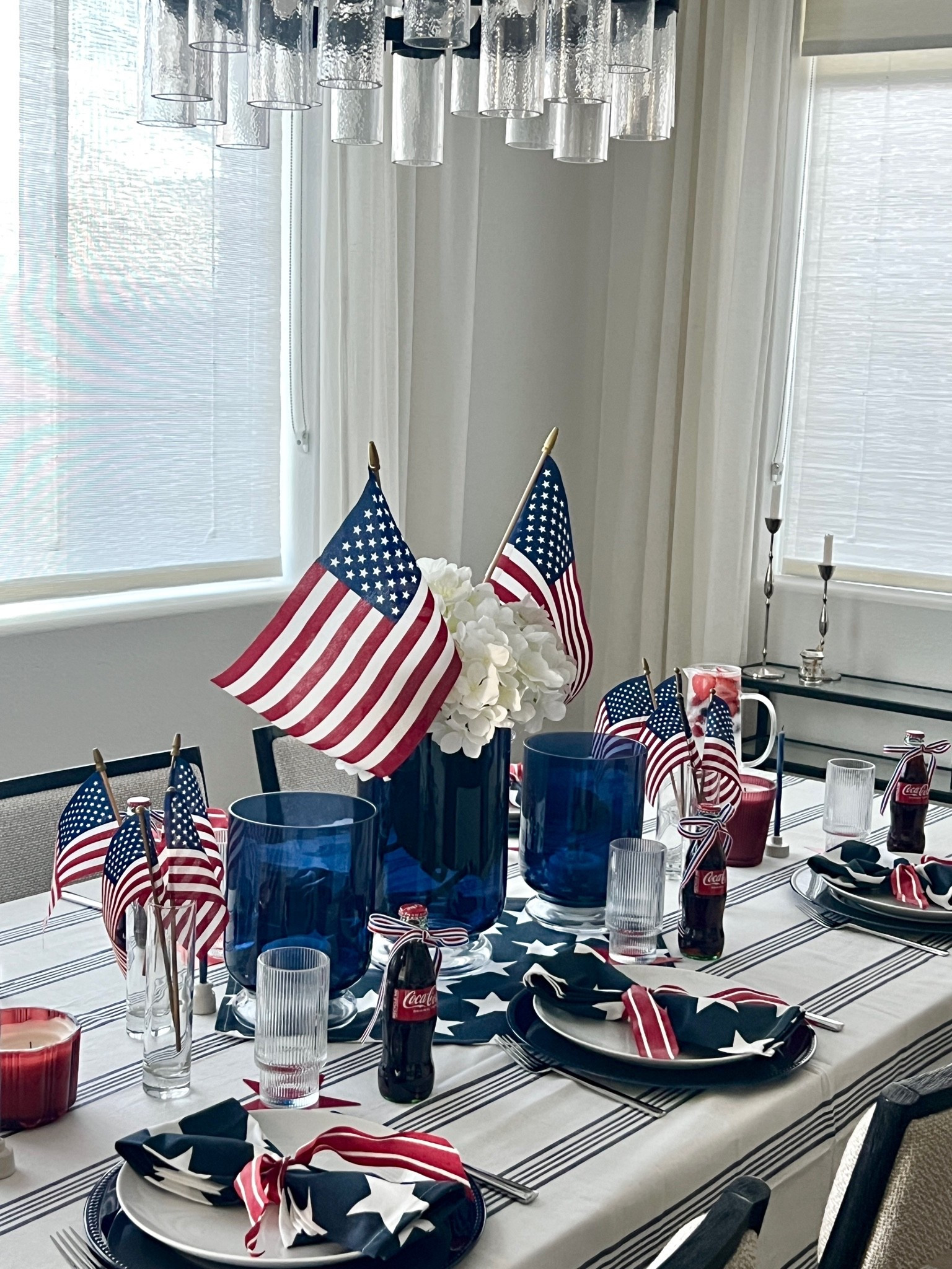 Americana table decor, patriotic tablescape, Memorial Day table setting, 4th of July table ideas, red white and blue decor, striped tablecloth, star napkins, patriotic napkin rings, navy blue plates, white dinner plates, layered table setting, ribbed drinking glasses, blue glass vases, hydrangea centerpiece, American flags table decor, mini flags centerpiece, red candle holders, taper candles neutral holder, coke glass bottles vintage style, ribbon tied bottles, patriotic cake stand, hosting table ideas, summer hosting decor, classic Americana style, modern patriotic table

#LTKHome #LTKSeasonal
