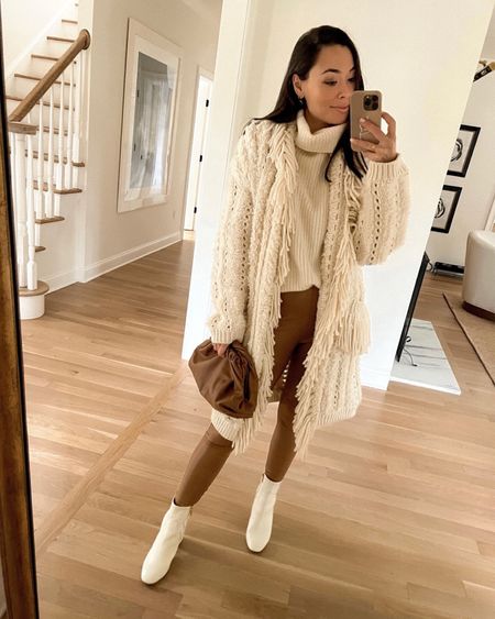 Kat Jamieson of With Love From Kat wears a winter outfit. Fringe cardigan sweater, cashmere turtleneck, brown faux leather leggings, white leather booties, brown clutch, classic style, neutral style.

#LTKstyletip #LTKshoecrush #LTKSeasonal