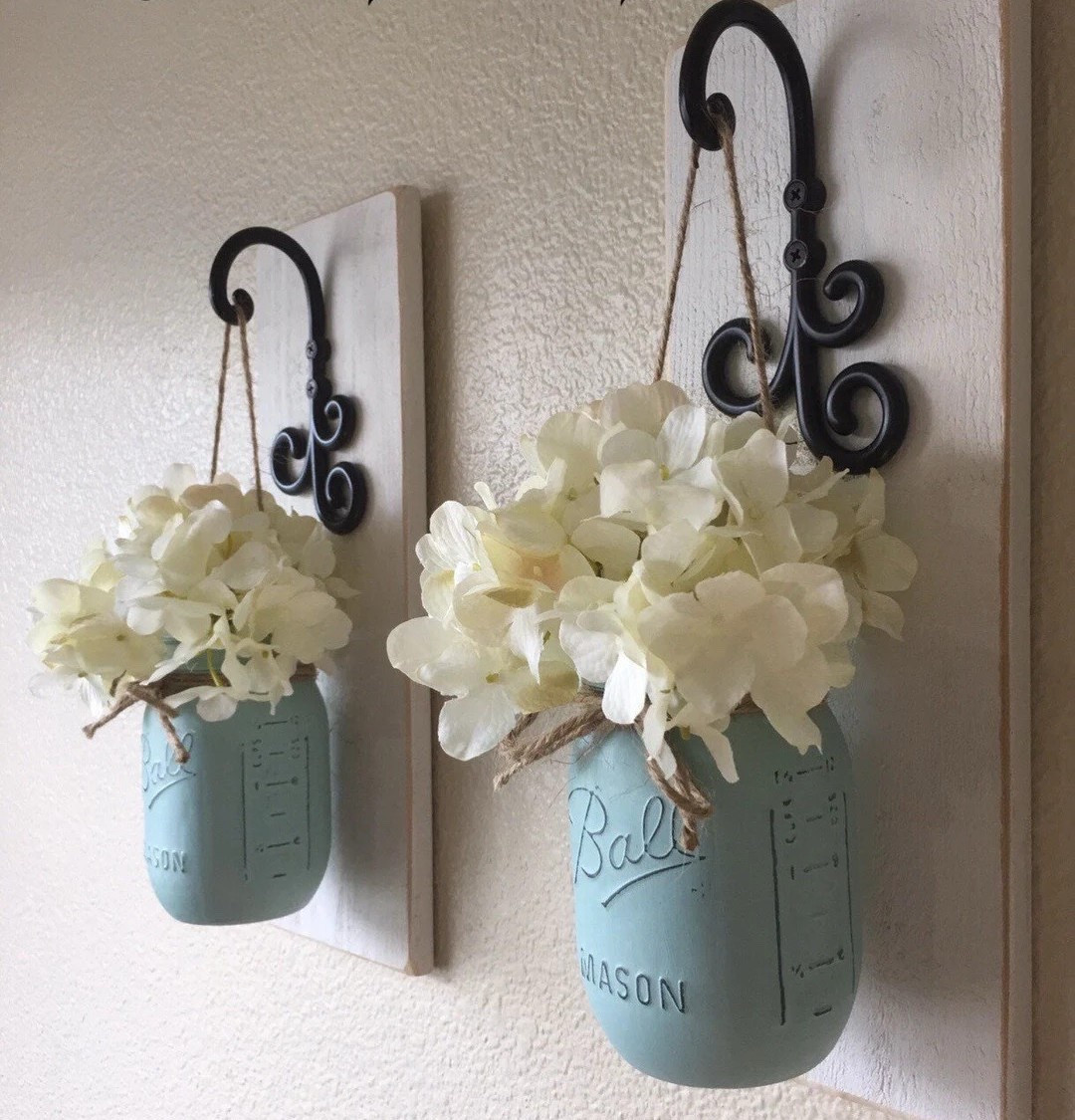 Bring cozy country charm into your home with these rustic mason jar sconces by CountryHomeandHeart. Featuring beautifully painted seafoam blue jars, antique white wood backing, and natural jute accents, this set of two creates a soft, welcoming glow in any space. Perfect for adding farmhouse warmth to hallways, bedrooms, or living areas, these sconces blend vintage style with a fresh, airy color palette. #LTKHome #FarmhouseDecor #MasonJarDecor #RusticStyle #CozyHome #WallSconces #CountryLiving #HomeInspo

#LTKWedding #LTKHome #LTKSeasonal