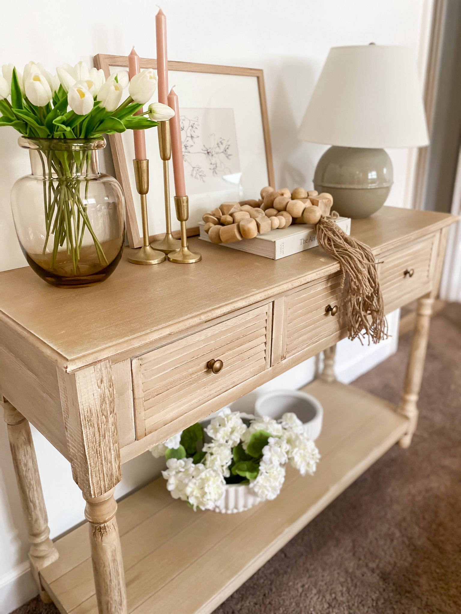 Console table styling idea!!! Spring console table decor, white tulips, amazon viral tulips, green lamp, brass hold candle holders, viral Walmart planter, white bowl, decorative bowl, wooden garland, the art of home book, console table, amber glass vase, flower vase, flower arrangement, picture frame, wallart, organic modern home, coastal home, living room, living room decor 

#LTKstyletip #LTKSeasonal #LTKSpringSale