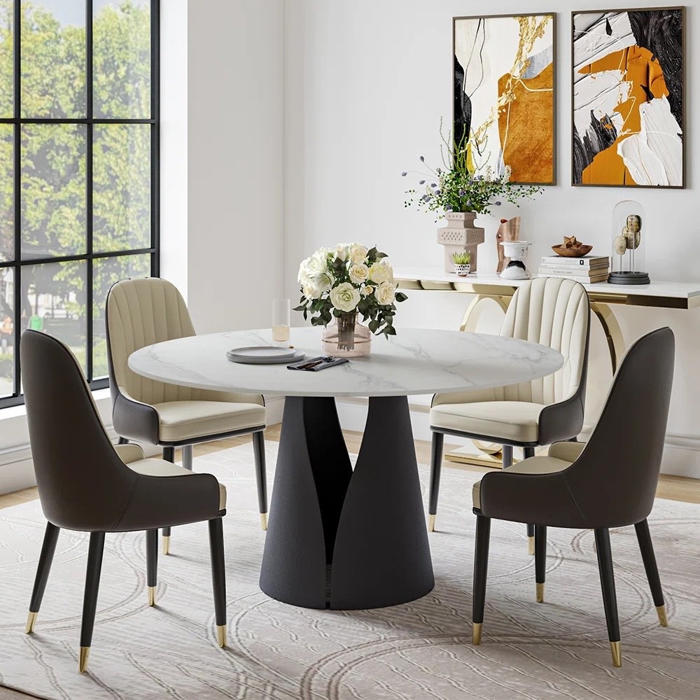 This round dining set from Wayfair has such a polished look without making the room feel too formal. The white sintered stone tabletop with the sculptural black pedestal base really stands out, and the upholstered dining chairs soften everything up with their curved backs and channel stitching. I also like how the neutral area rug, white floral centerpiece, gold-accent console, and abstract wall art pull the whole dining room together. It comes in 5-piece and 7-piece options depending on how much seating you need.