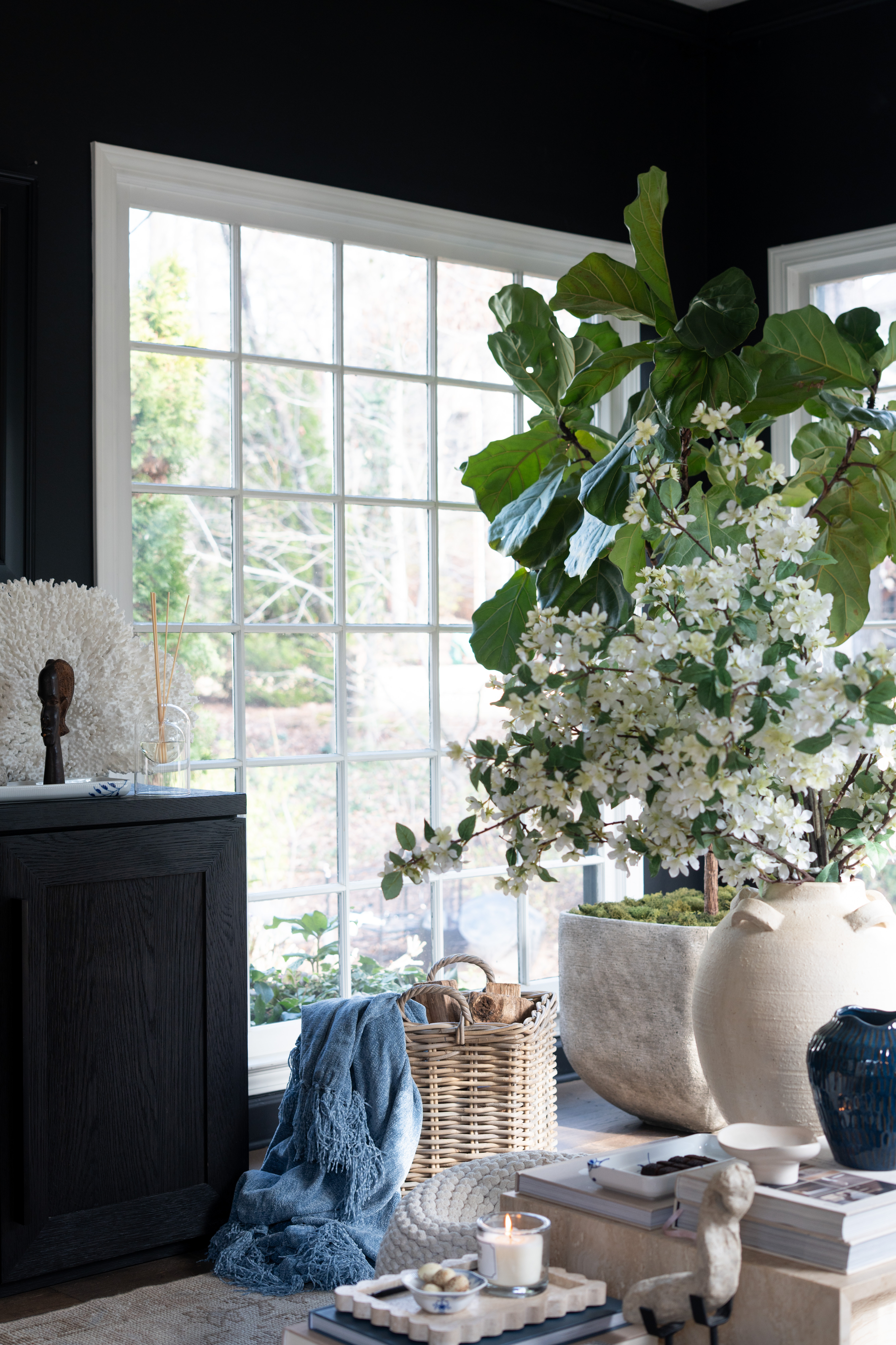 The sunlight in this corner makes everything feel extra cozy. The oversized vase filled with spring blossoms, layered coffee table books, candle glow, and marble table styling create the most beautiful little moment. I love how the soft neutrals, natural textures, and subtle blue accents make the whole space feel calm, warm, and effortlessly styled. 

 #LTKSpringSale #LTKSeasonal #LTKHome