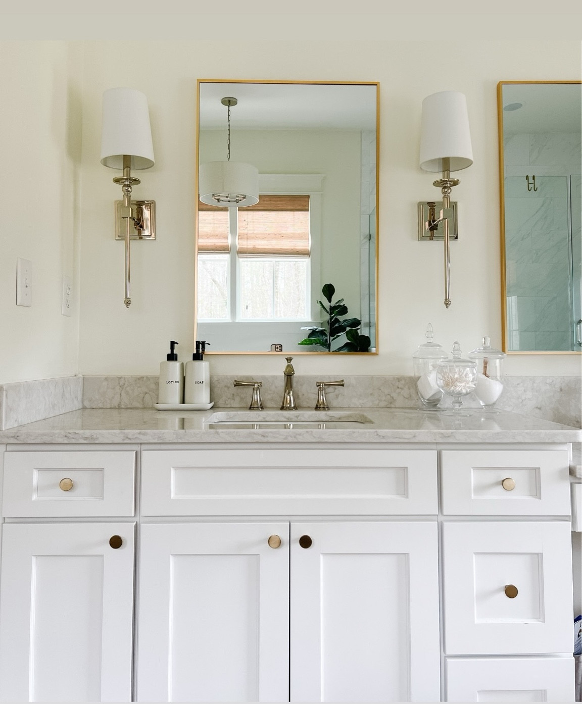A view of our primary bathroom. I love the modern gold mirror and traditional style polished nickel sconces we used. We mixed metals between gold on the hardware & mirrors and polished nickel on the faucet and fixtures. 