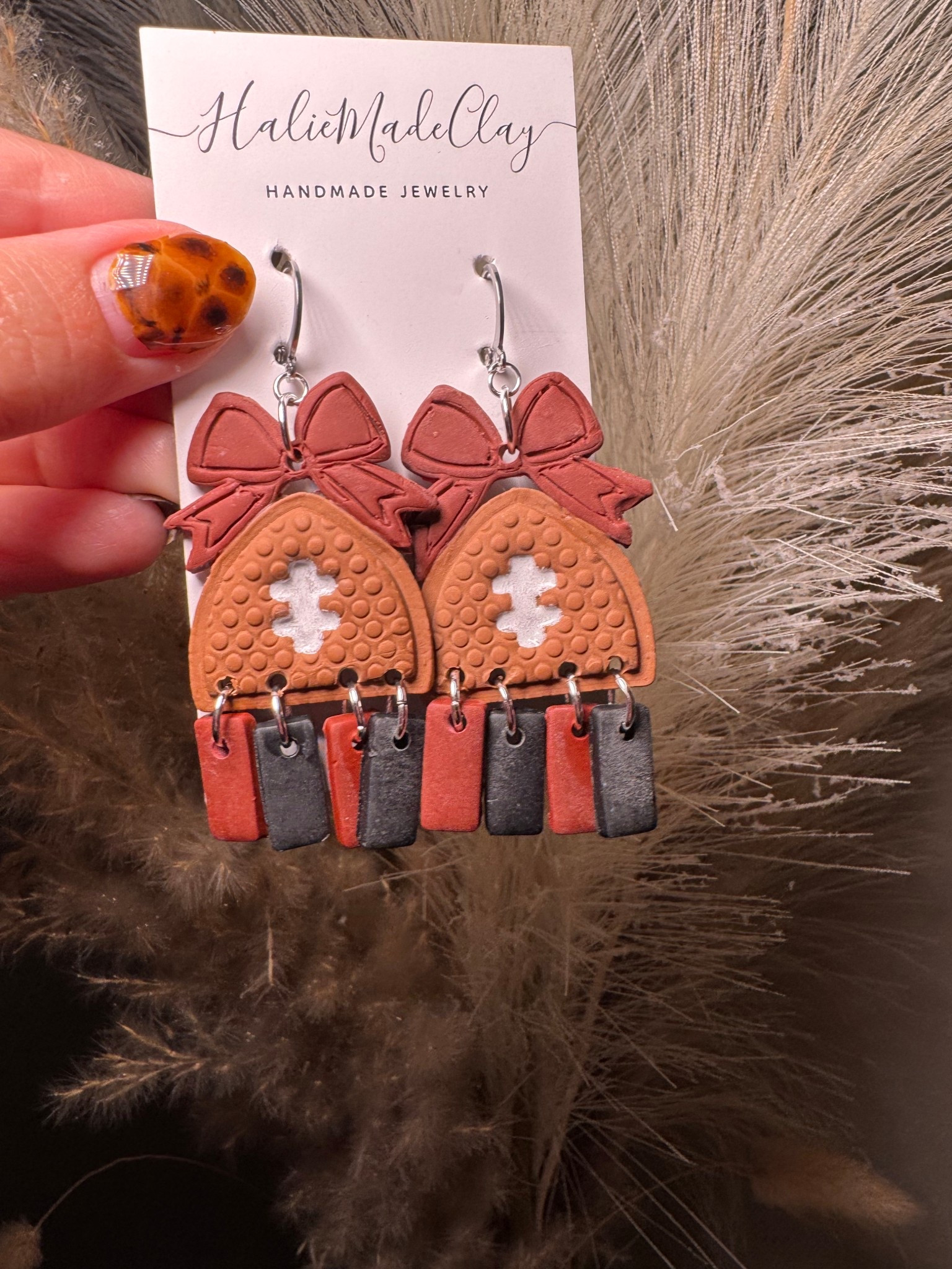 Cheer in style! These handmade polymer-clay football earrings feature a textured “pigskin” dome with hand-painted laces, topped with a sweet bow and finished with swingy tassel tiles for extra movement on game day. Each pair is crafted by hand in small batches—lightweight, comfortable, and perfect for tailgates, Friday nights, and NFL Sundays.

Highlights
	•	Handmade in Kentucky by HalieMadeClay
	•	Ultra-light polymer clay (comfortable for all-day wear)
	•	Sealed for durability; satin finish
	•	Shop small • Woman-owned

Details
	•	Materials: Polymer clay, stainless steel hooks, jump rings, acrylic paint/sealant
	•	Color: Warm football brown with white laces; tassels in brown + white; coordinating clay bow top
	•	Texture: Raised “football” pebble texture
	•	Back: Smooth, sanded

Size & Weight (approx.)
	•	Drop length: 2.25–2.5 in (57–63 mm) from top of hook
	•	Width: 1.0–1.1 in (25–28 mm) at widest point
	•	Weight: ~0.15–0.20 oz (4–6 g) per earring

Variations / Custom

Want school or team colors for the tassels or bow? Choose Custom Colors at checkout and add your colors in the personalization box (two colors max). I’ll send a quick proof before making.

Care

Store flat and away from heat. Avoid bending. If needed, wipe gently with a soft, slightly damp cloth. Keep away from perfumes/lotions.

Packaging & Gifting

Arrives on a branded card in a protective pouch—gift-ready. Add a gift note at checkout!

Processing & Shipping
	•	Processing time: 3–5 business days (custom colors: 5–7 days)
	•	Ships via USPS with tracking. 

Returns/Exchanges

Hygiene-safe returns accepted within 14 days in original condition. Custom color orders are final sale, but please contact me if there’s any issue—I want you to love your earrings!

—
Handmade means every pair is unique; slight variations in texture and color are part of their charm.

#LTKSeasonal #LTKKids #LTKGiftGuide