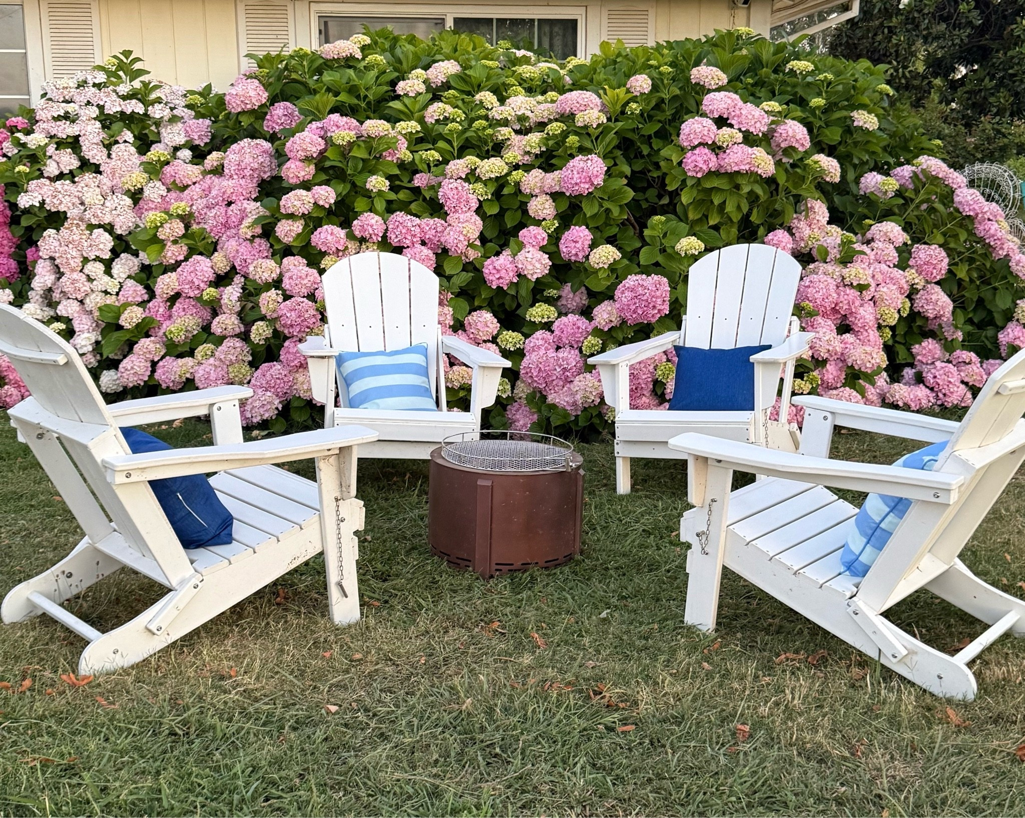 #ad My gorgeous coastal inspired garden renovation courtesy of @Wayfair! I love these white folding Adirondack chairs! They look great around my smokeless fire pit! I adorned the chairs with solid blue and blue striped outdoor throw pillows in my hydrangea garden! This is perfect for summer and Father’s Day weekend!! #wayfairpartner #wayfair #wayfairpicks

#LTKdayinmylife #LTKHome #LTKSeasonal