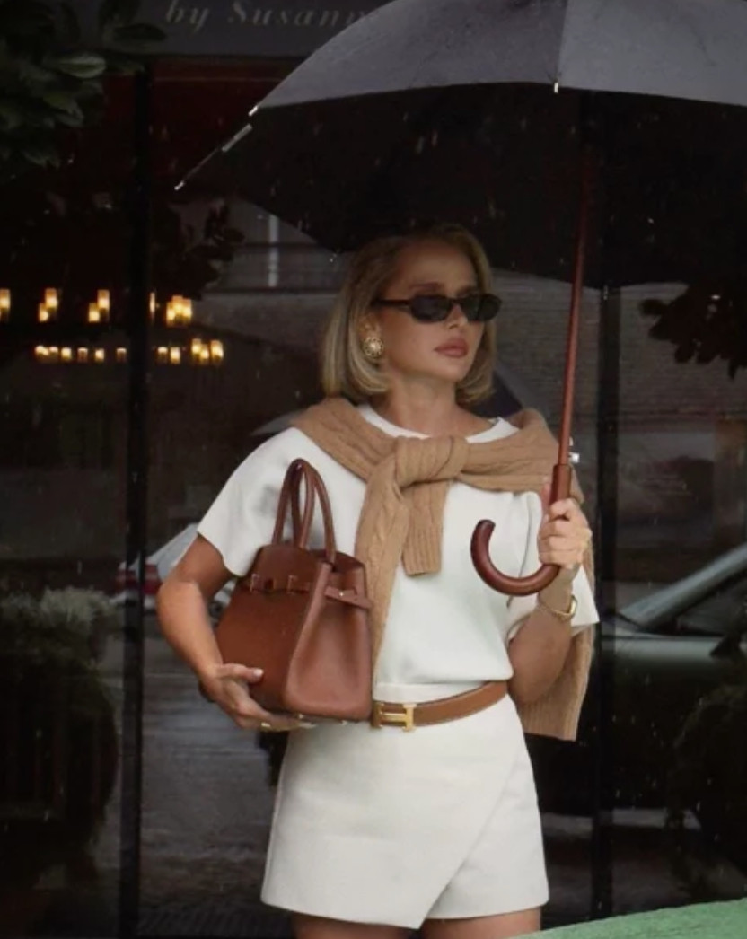 Elevated casual outfit with a white t-shirt, tailored shorts, brown leather belt, sweater draped over the shoulders, and a structured handbag for a chic, polished everyday look.
Style tip: pair simple basics like a white tee and tailored shorts with elevated layers like a sweater over your shoulders, and add classic accessories like a leather handbag, belt, and sunglasses to create a timeless, old money inspired outfit that feels effortless but put together. 

 #LTKootd