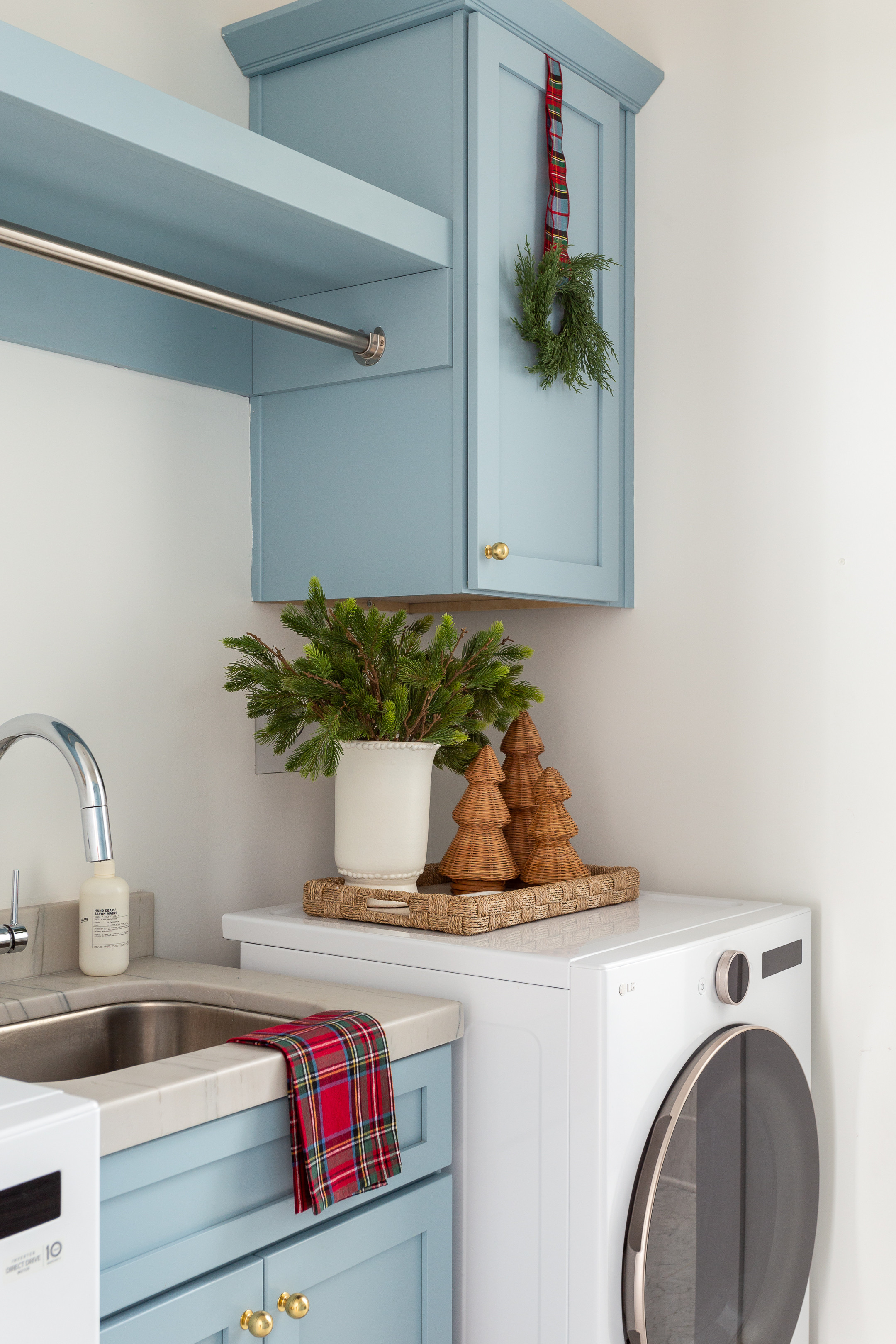 Our laundry room decorated for Christmas. I hung a mini cedar wreath with plaid ribbon on our blue cabinets, added a red Stewart plaid tea towel, vase with faux evergreens, rattan Christmas trees and a woven tray to add a festive touch! See more pics and our full Christmas home tour here: https://lifeonvirginiastreet.com/2024-christmas-home-tour/ #ltkhome #ltkholiday #ltkfindsunder50 #ltksalealert #ltkseasonal #ltkfindsunder100 #ltkstyletip 

 #LTKHoliday #LTKHome #LTKFindsUnder50