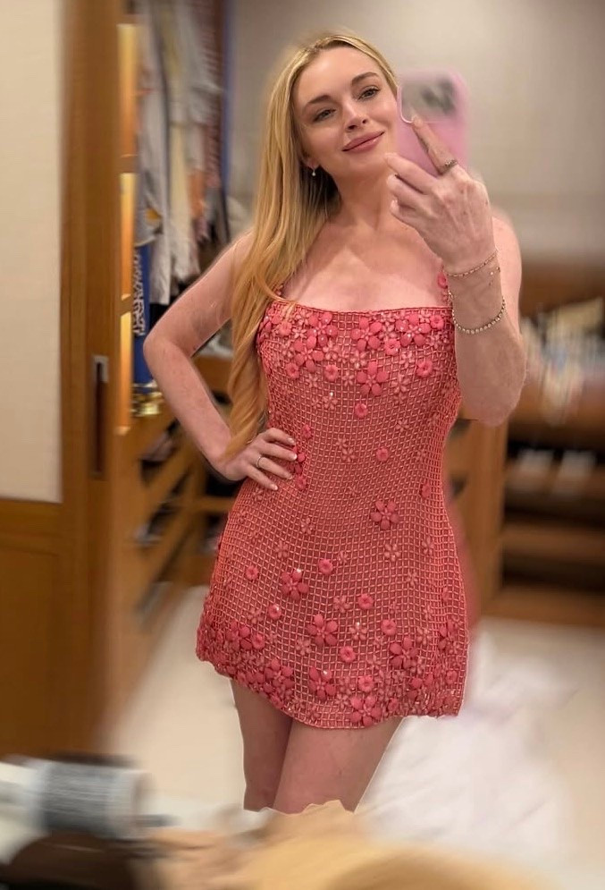 Lindsay Lohan wearing a strawberry pink delicate mini dress featuring intricate floral appliqué over a sheer grid base.