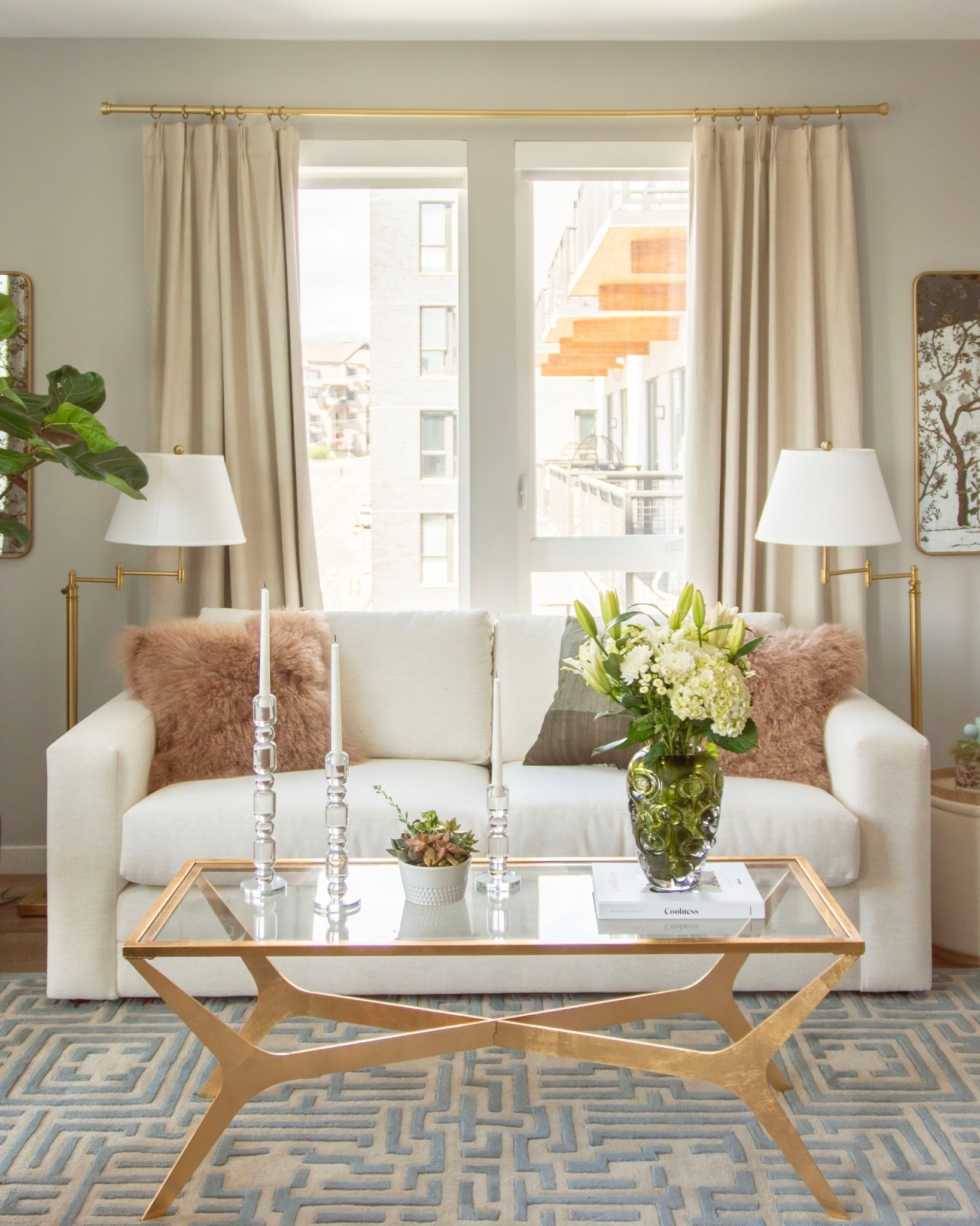 Classic apartment living room design with white sleeper sofa, gold coffee table, beige pleated curtains, and brass swing-arm floor lamps with home decor styling accessoriess

#LTKHome
