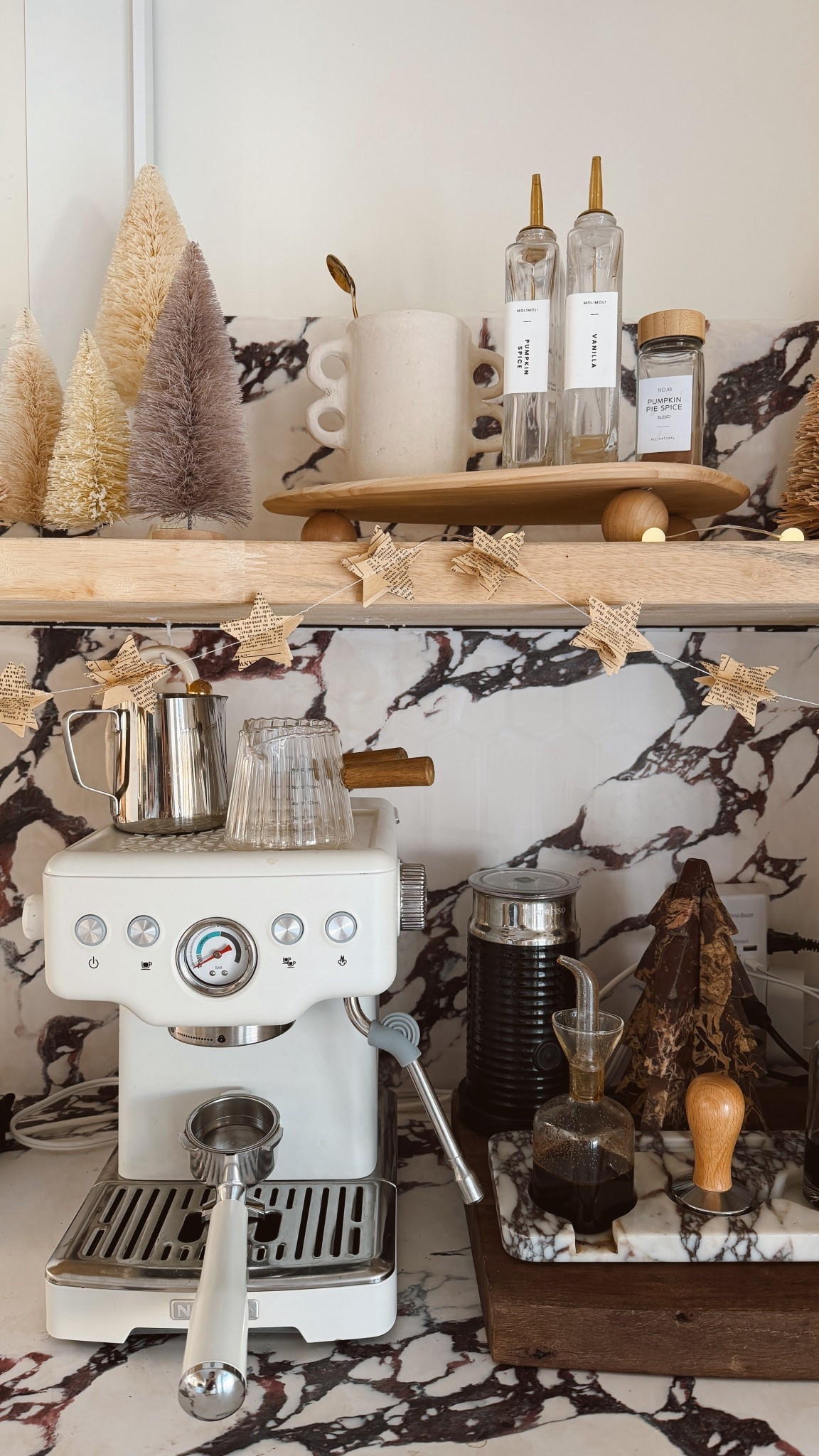 organic modern coffee bar, christmas coffee bar decor, neutral christmas decor, bottle brush trees, cozy kitchen styling, small kitchen coffee station, aesthetic coffee corner, holiday kitchen ideas, marble tray styling, neutral holiday aesthetic, espresso machine setup, kitchen shelf styling, wooden riser decor, glass syrup bottles, modern cottage kitchen, countertop decor ideas, cozy home inspiration