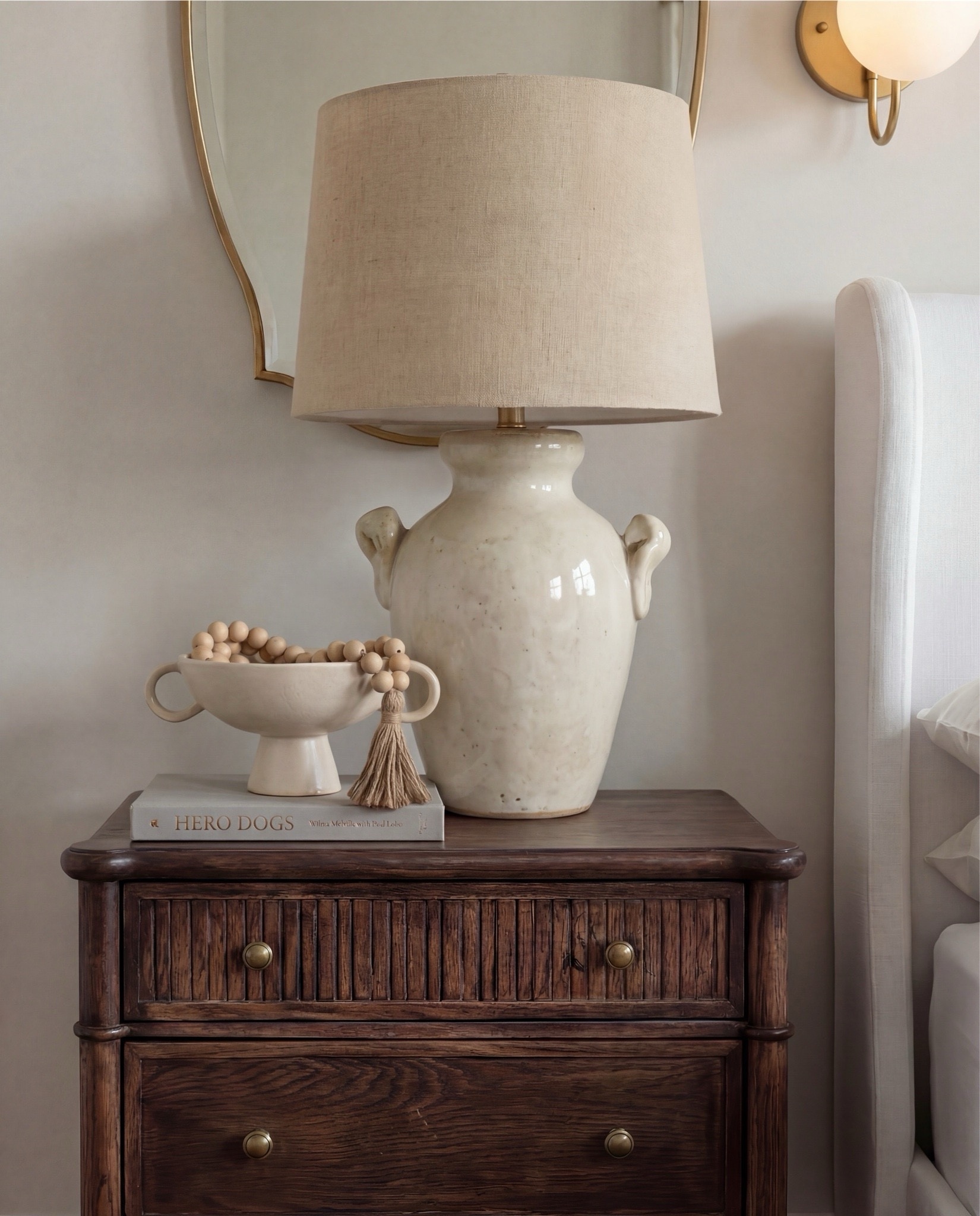 Shop the Look:
• White upholstered wingback bed frame
• White cotton duvet cover + pillow shams
• Textured throw pillows (rust + black patterned)
• Chunky knit throw blanket (warm brown)
• Vintage-style brown area rug
• Dark wood nightstands with brass knobs
• Ceramic table lamp (neutral glaze)
• Brass globe wall sconces
• Framed floral artwork (muted tones)
• Arched brass wall mirrors
• Upholstered bench at foot of bed (camel brown)
• Cream accent chair with wood arms
• Black fluted dresser with brass pulls
•Ceramic beige decor bowl
•Decor wood beads 
•Decor book
• Large ceramic floor table vase (earthy clay tone)
• Decorative wood bead garland
• Sheer white curtain panels
•Decor tray
•Hurricane candle holder
Wood Jewelery box 


#LTKSaleAlert #LTKHome