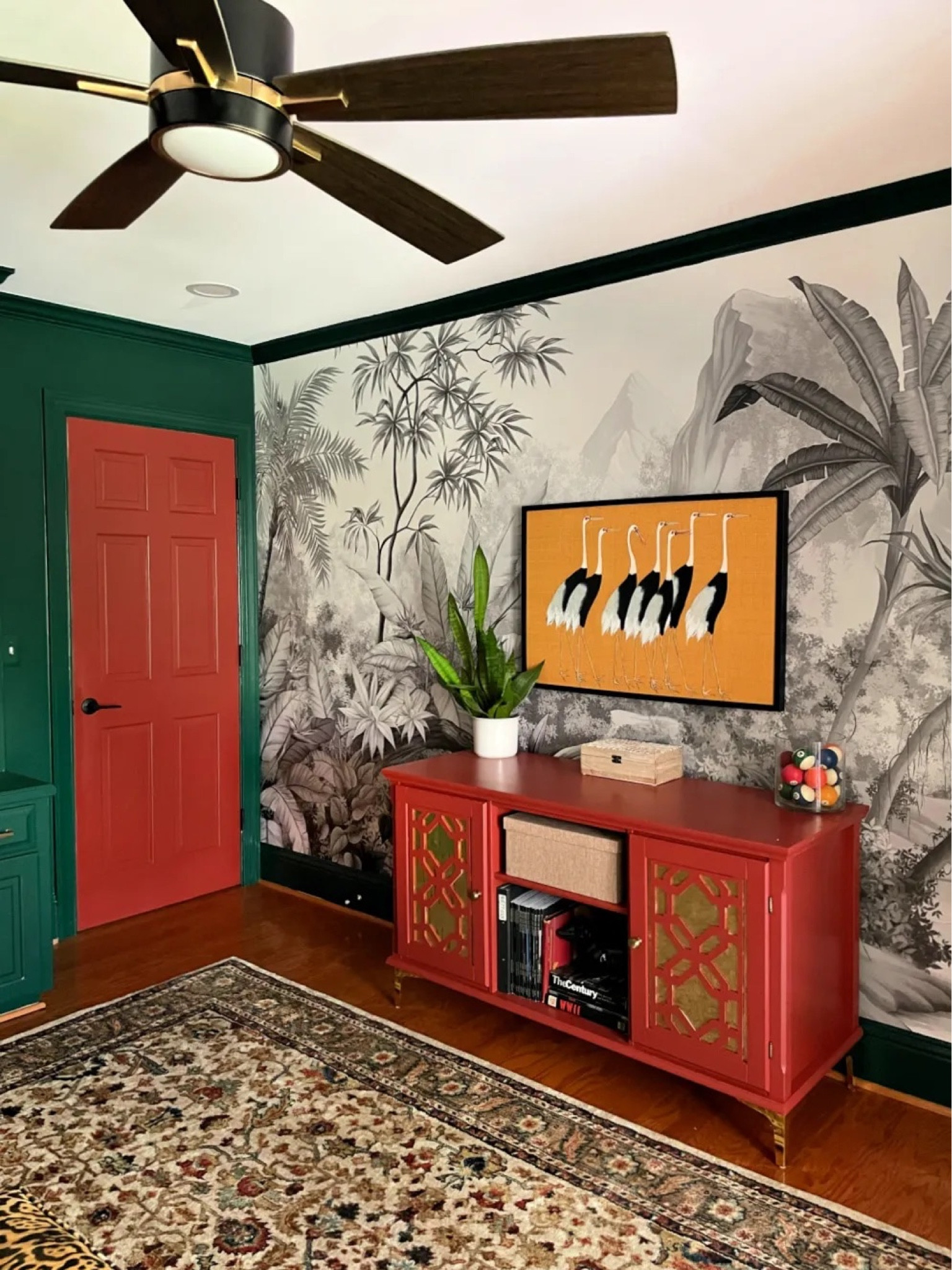 Jungle wallpaper, red tv cabinet, black ceiling fan, crane print, yellow art print, masculine decor, green rust rug

#LTKhome