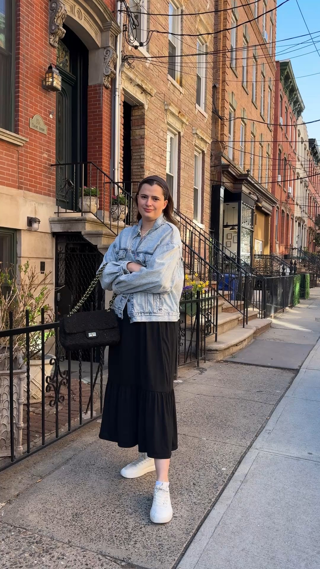City chic spring outfit idea  A mix of classic and contemporary with an oversized denim jacket layered over a black midi dress and classic white sneakers. This outfit balances comfort and style, making it ideal for a springtime stroll in the city.