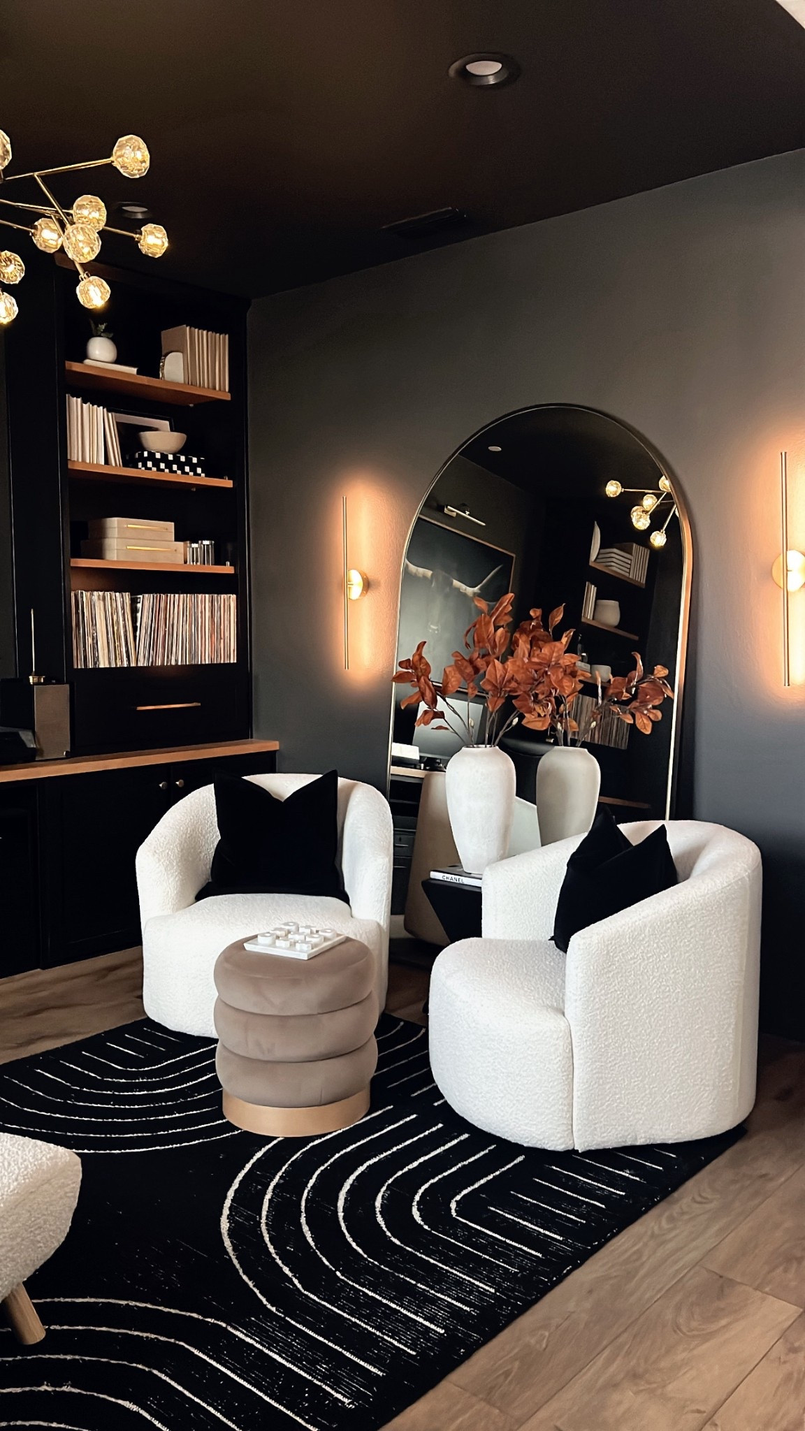 A den - but let’s make it moody! Paint is urban bronze by Sherwin-Williams. Black and white hand tufted rug, oversized arched wall mirror, brown velvet ottoman, swivel chairs, moody den decor, remote wall sconces, 

#LTKHome