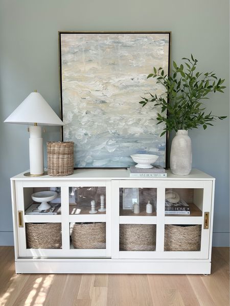 Off white, brass, and glass cabinet. Media cabinet. Buffet. Office storage. Woven round baskets are size large and perfect for toy storage. White modern table lamp from target. Coastal seaside art in 40x50” with gallery aged brass frame 

#LTKsalealert #LTKhome #LTKstyletip