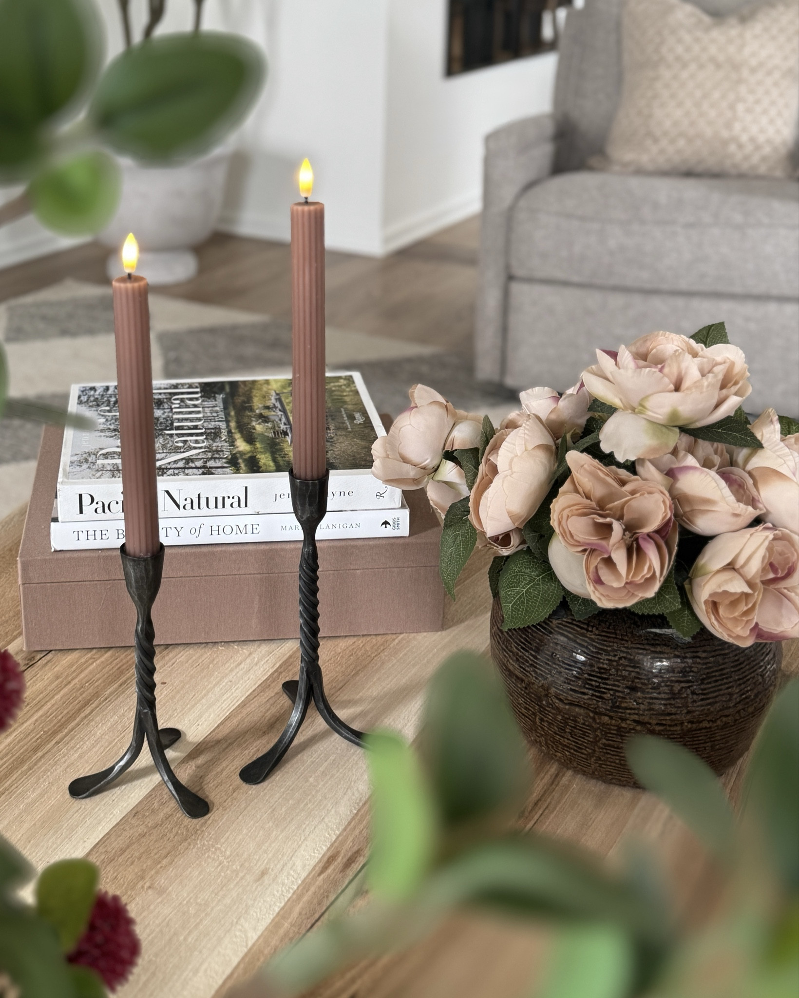 Spring vignette with spring florals, aged vintage bean pot, my fave new 7’ olive tree, 20” large and wide planter great for taller trees, 3-legged solid wood accent table, white ceramic vase, two different sets of peonies, coffee table books, black iron roped candle holders, ribbed battery operated taper candles, reclaimed wood coffee table, neutral area rug  