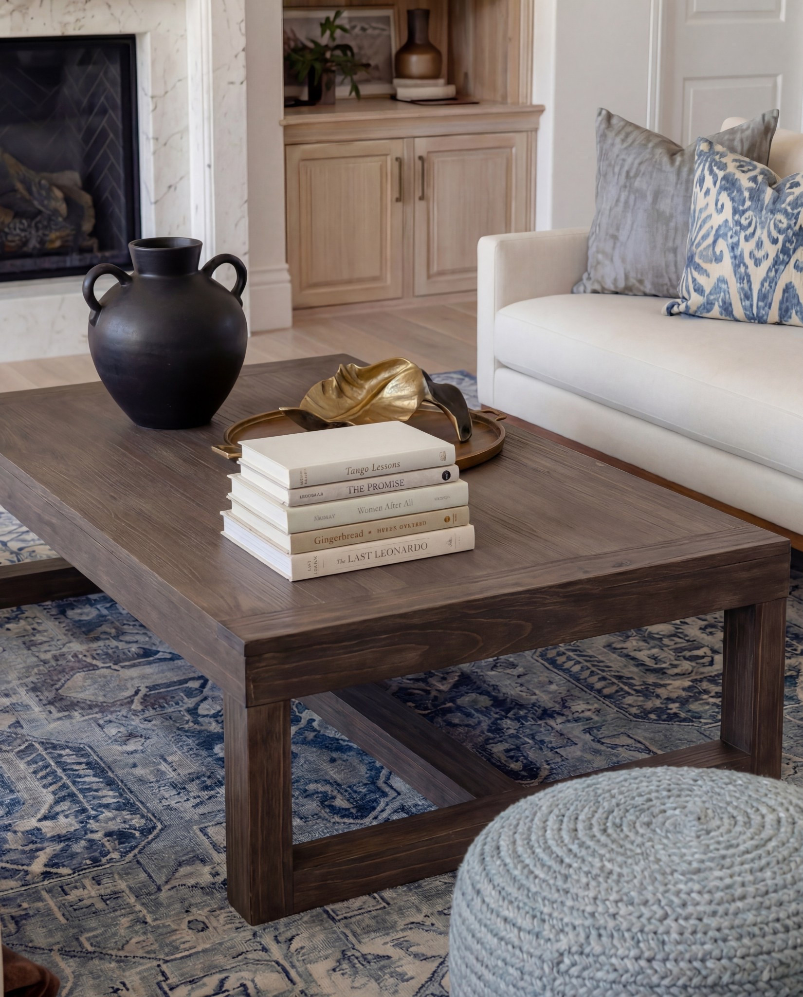 Shop the Look:
• Marble fireplace surround
• Cream armchairs + sofa
• Blue patterned lumbar + throw pillows
• Chunky knit ottomans
• Solid wood coffee table
• Black ceramic vase decor
• Distressed blue traditional rug
• Wood built-ins with glass fronts
• Warm wood ceiling beams
Brown throw blanket 
White decor books
Brass oval tray
Black decor bowl
Rounded globe chandelier 

#LTKSaleAlert #LTKHome #LTKFindsUnder100