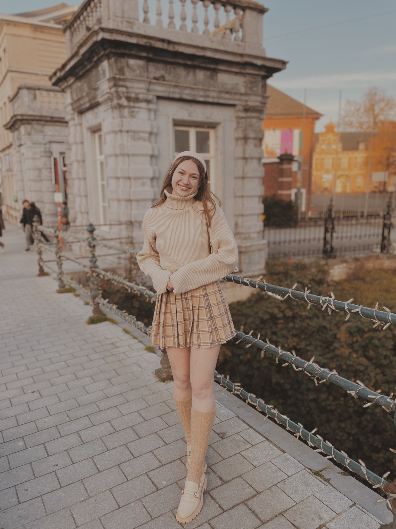 Beige knitted turtleneck sweater 
Beige pleated checkered skirt 
Light brown cable knit knee high socks
Beige loafers with gold detail
Beige knitted headband 