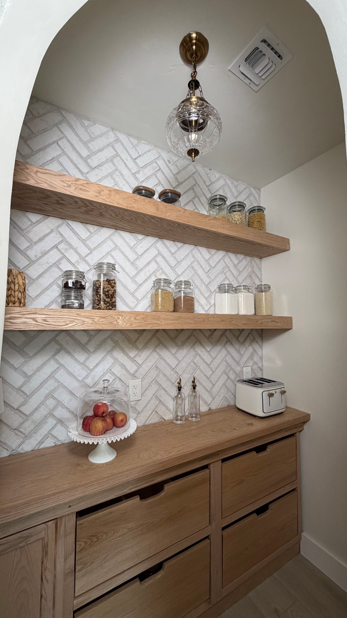 Pantry makeover with thin brick in a herringbone pattern, silver grout, floating red oak shelves + warm brass lighting. This completely changed the feel of the space!

Thin brick is “Cascade” by Old Mill Building Products  