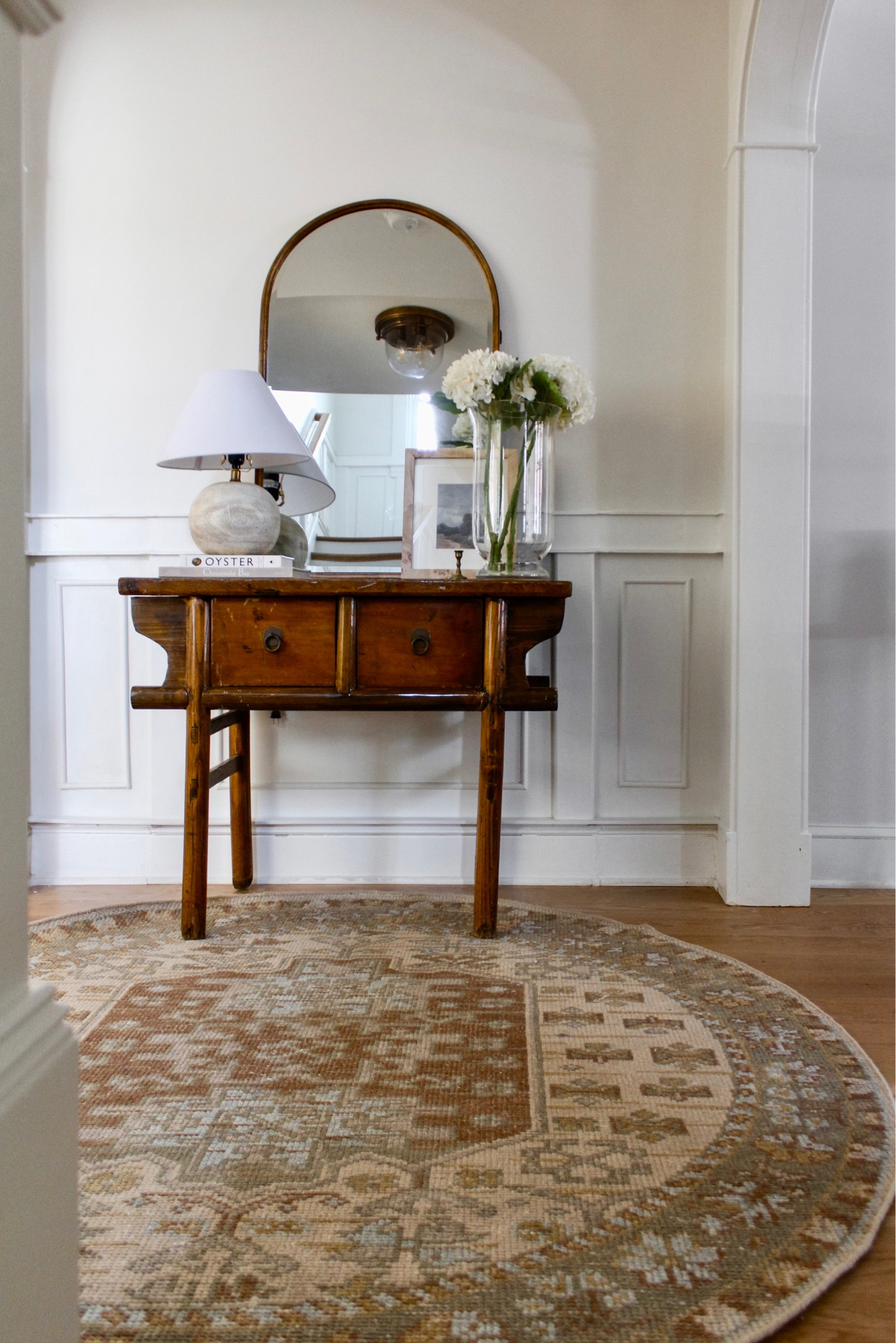 Waiting for the pieces that make your heart sing is what makes spaces come together to feel like home 🤍 This new beauty from @potterybarn has the best mix of muted earth tones - shop via the link in bio ✨ (gifted)
•
Shop this entire space there, too!
•
•
• 
hallway decor, entry decor, console decor, vintage console, table styling, home decor, simple home decor, neutral decor, arch mirror, spring summer florals, faux hydrangeas, lamp, round rug, loloi rug, affordable home decor, art print, burl wood frame, vintage art, woven rug, round rug #handknottedrug #woolrug